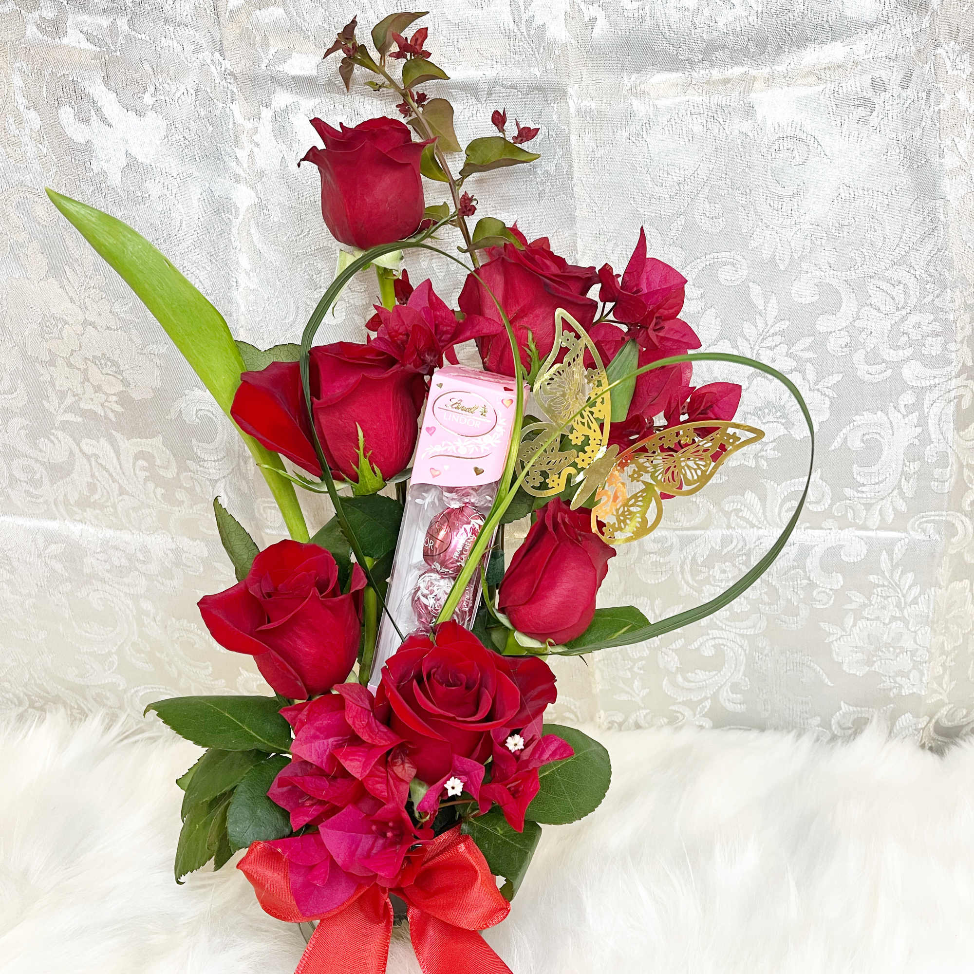 Red roses arranged with pink flowers, a ribbon, and a chocolate box