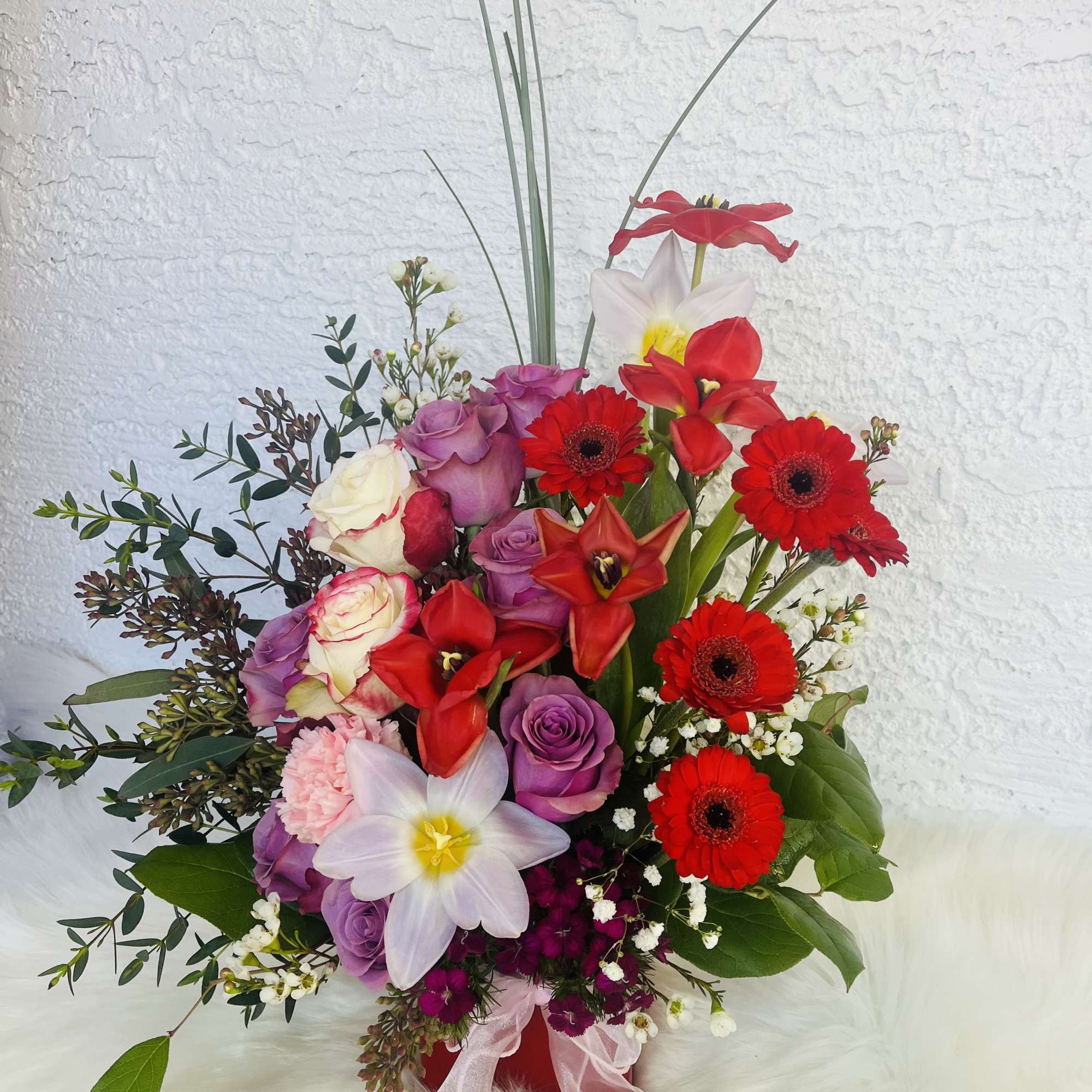 Mixed bouquet with red gerberas, roses, and white daffodils in a red vase