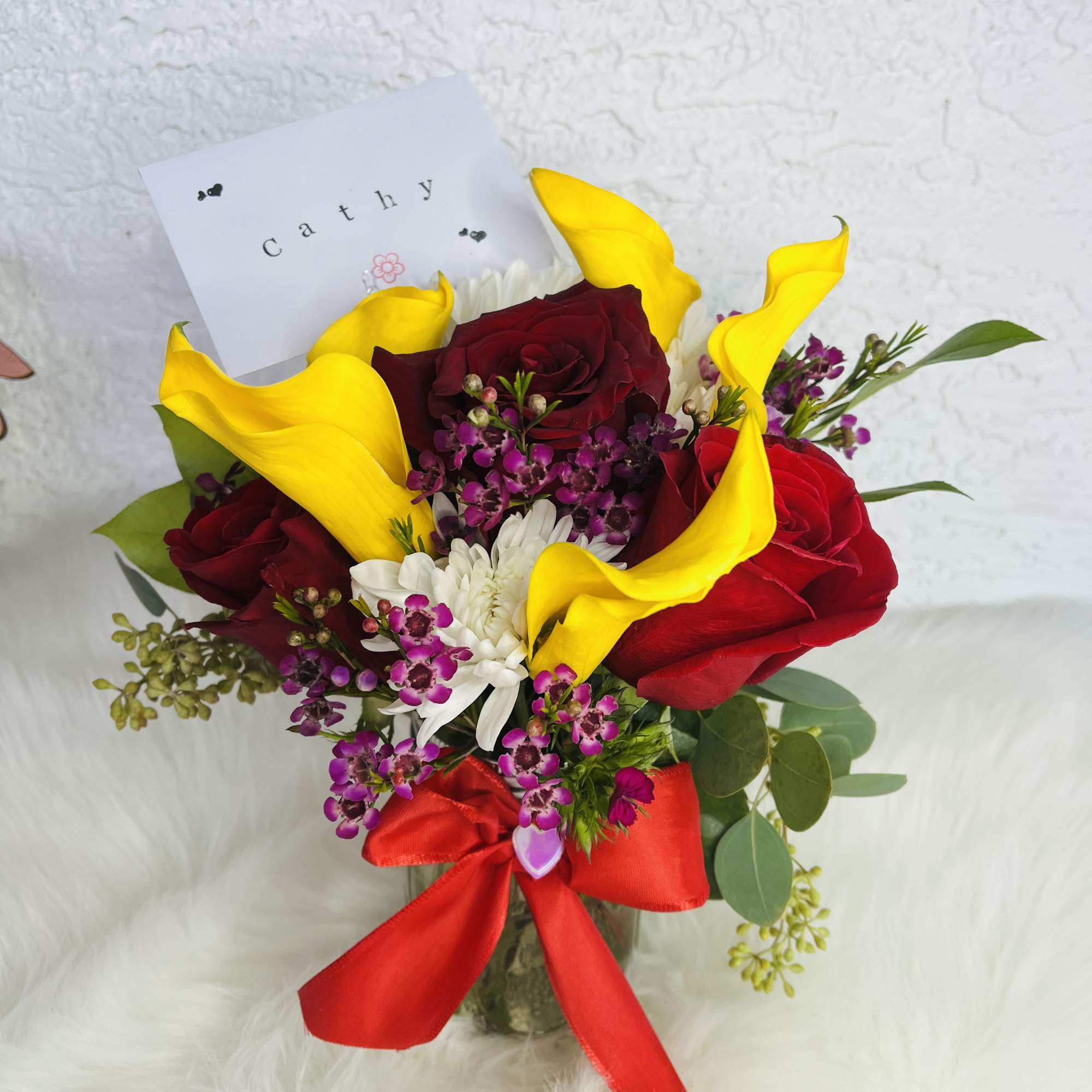 Bouquet of red roses, yellow calla lilies, and white flowers with a red ribbon
