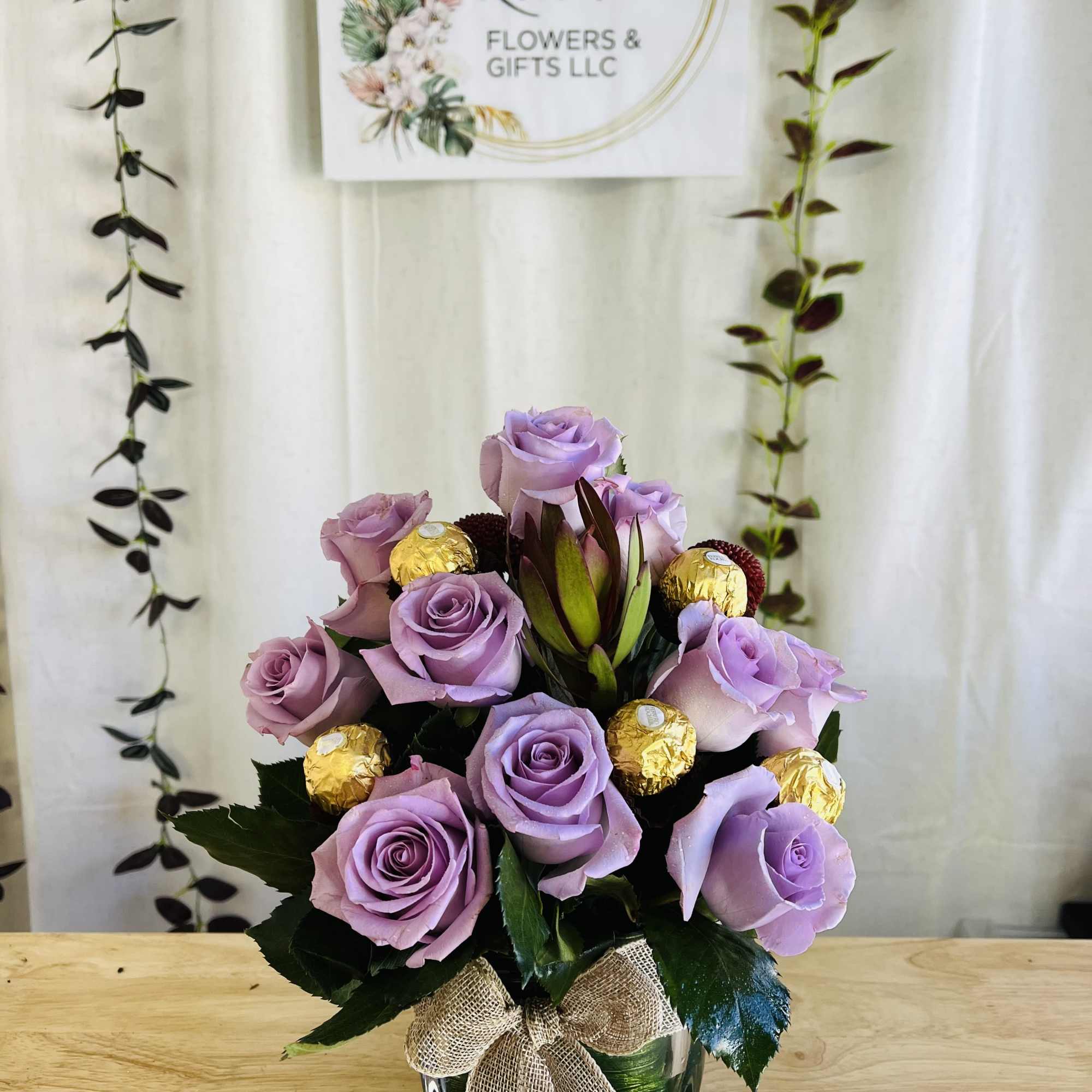 Lavender rose arrangement in a glass vase with gold-wrapped chocolates