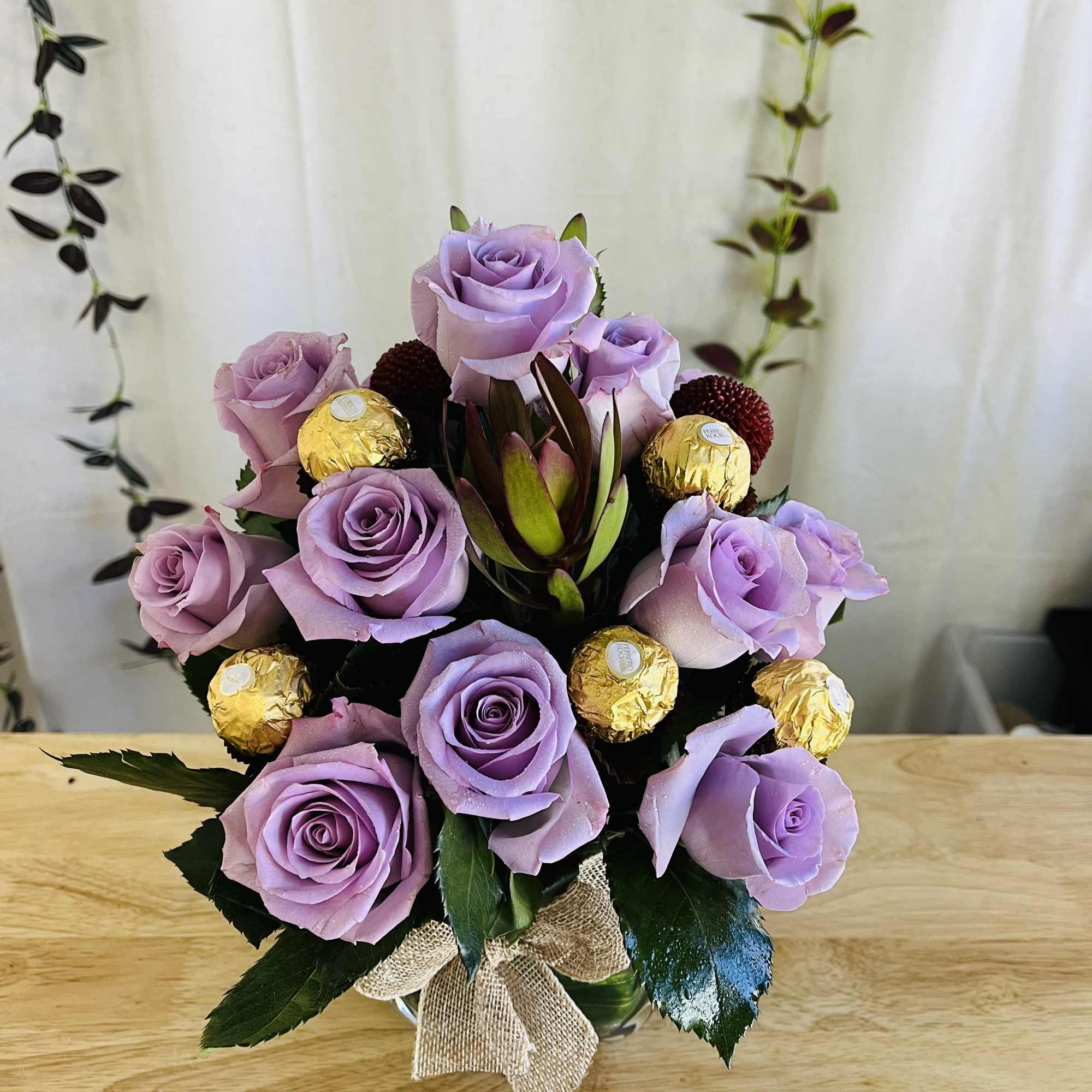 Lavender rose bouquet with gold-wrapped chocolates in a glass vase