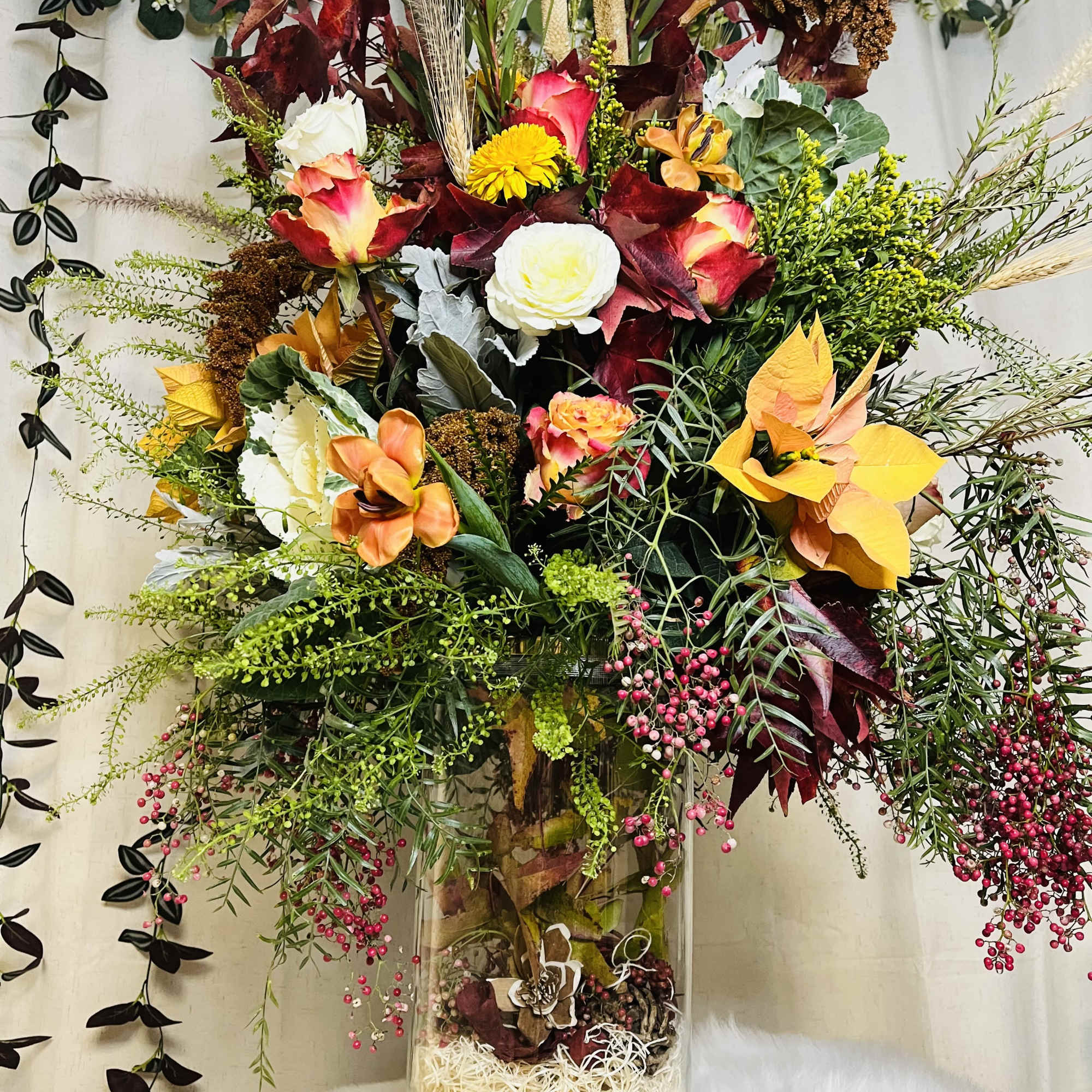 Tall mixed floral arrangement in a clear glass vase with autumn colors