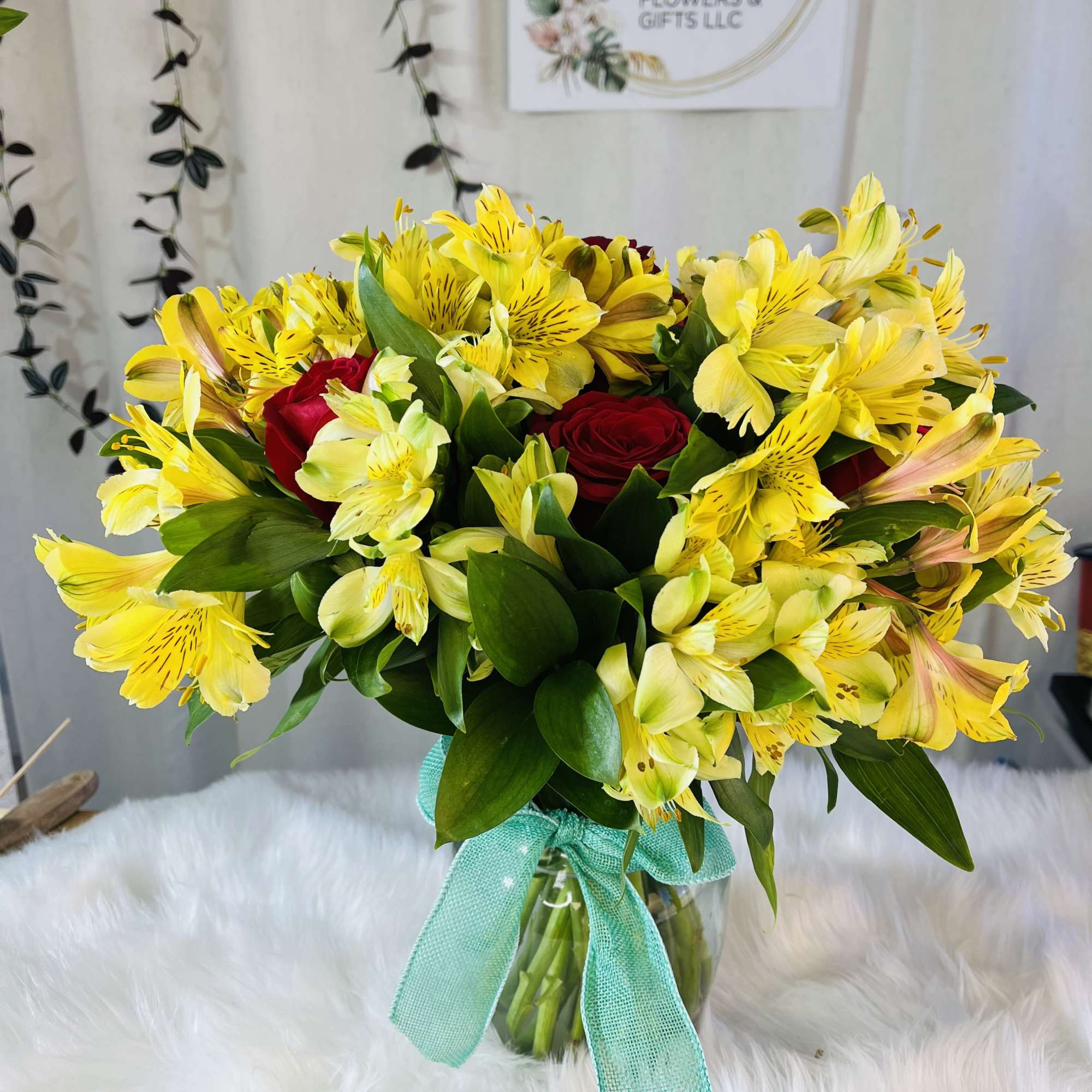 Yellow alstroemeria and red roses in a glass vase with a turquoise ribbon.