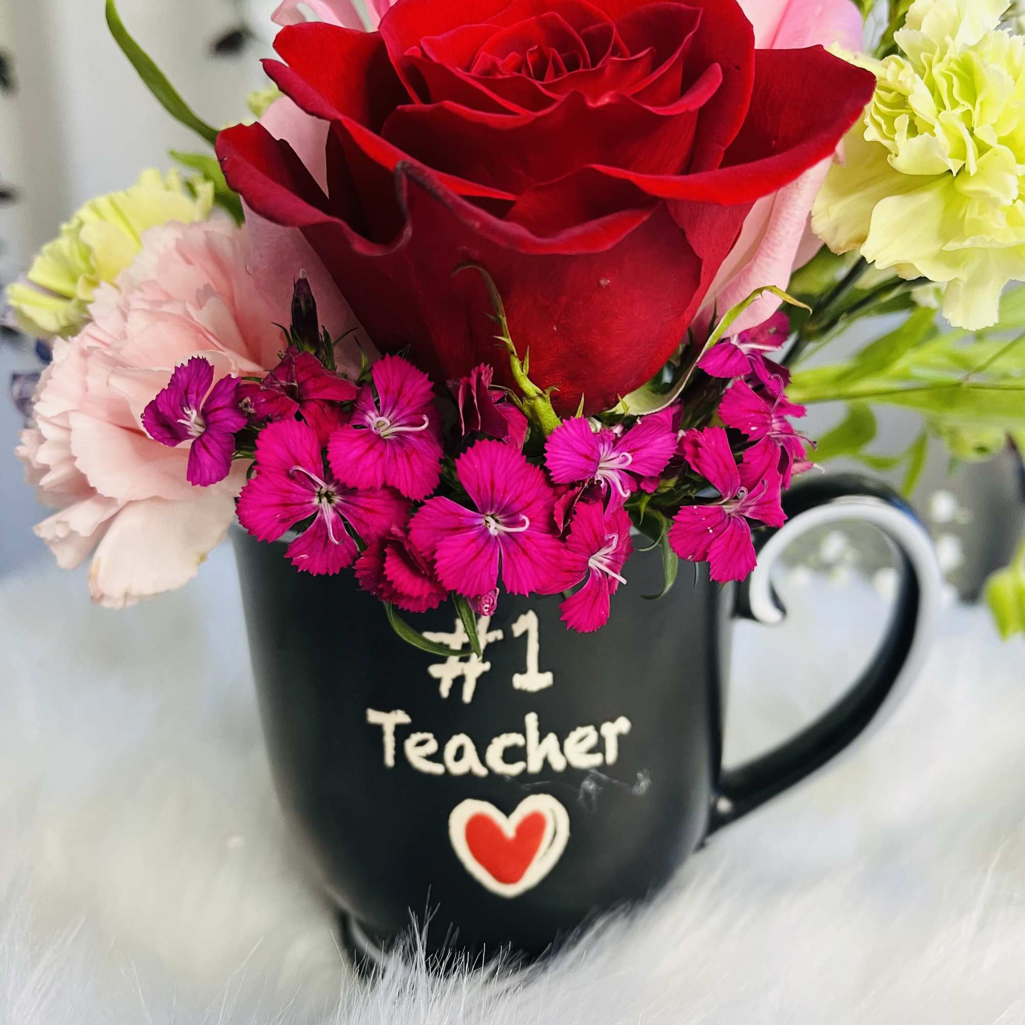 Mixed flowers arranged in a black mug labeled "#1 Teacher"