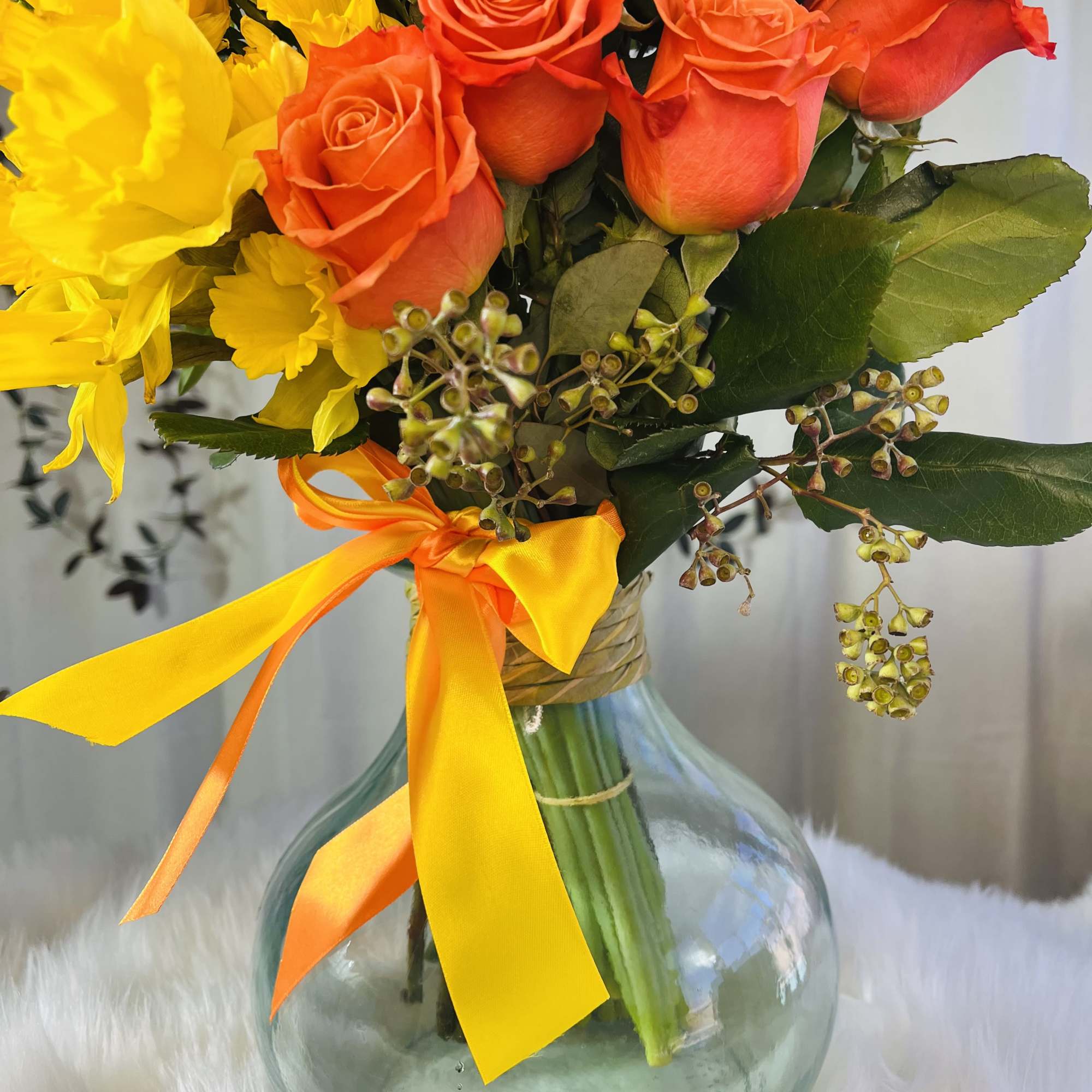 Orange roses and yellow flowers in a glass vase with a ribbon