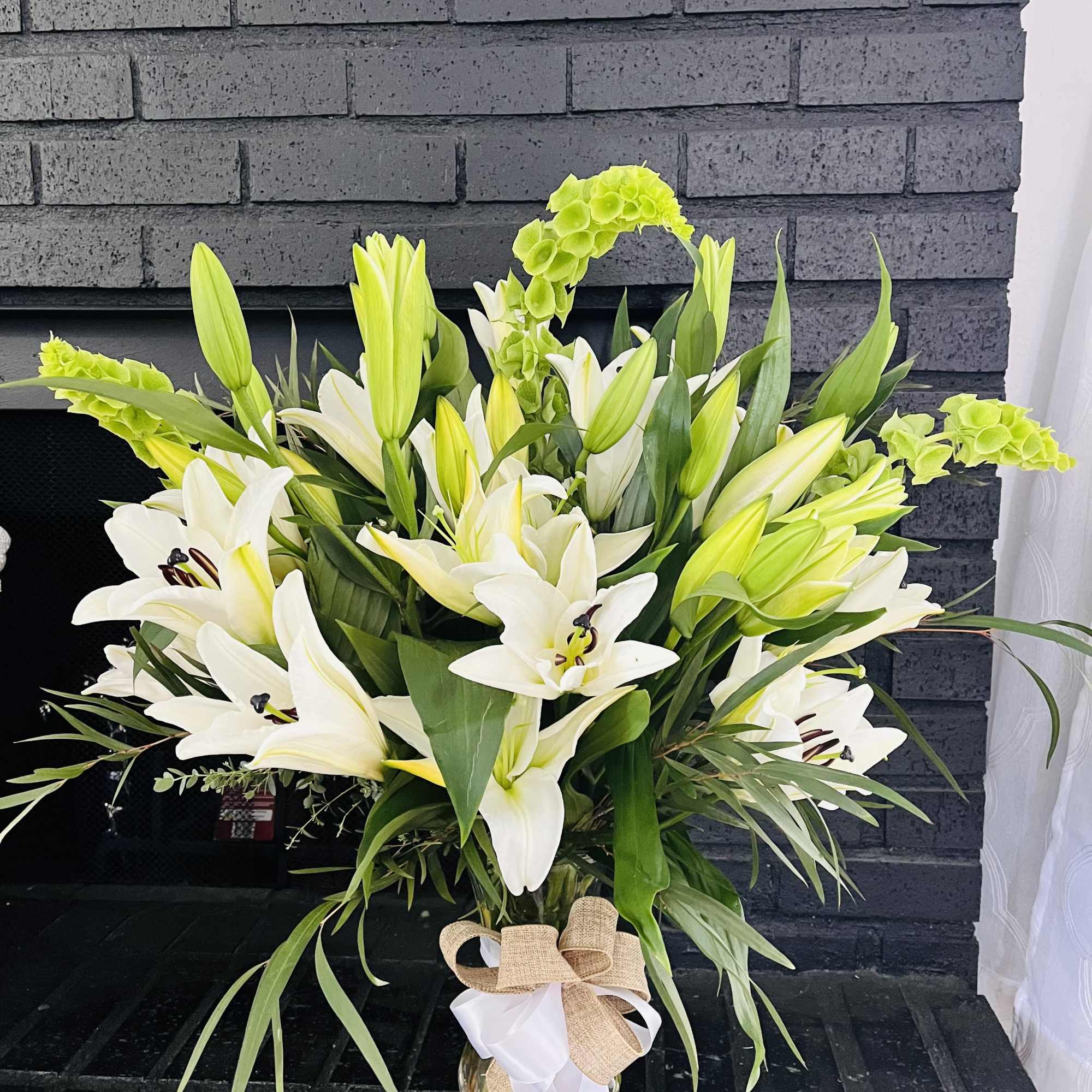 White lilies and green hydrangea in a glass vase with a burlap bow
