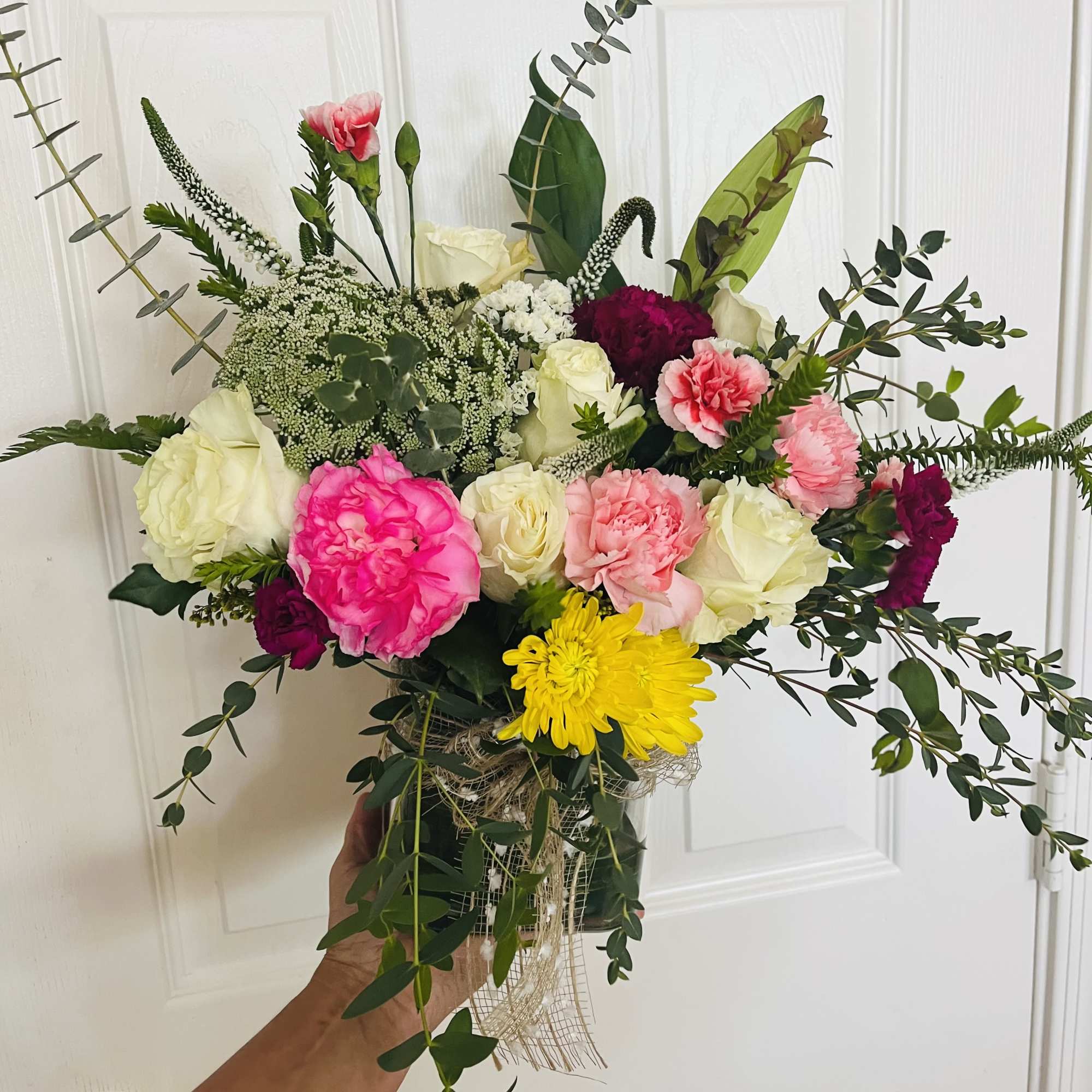 Handheld bouquet of pink, white, yellow, and burgundy flowers with greenery