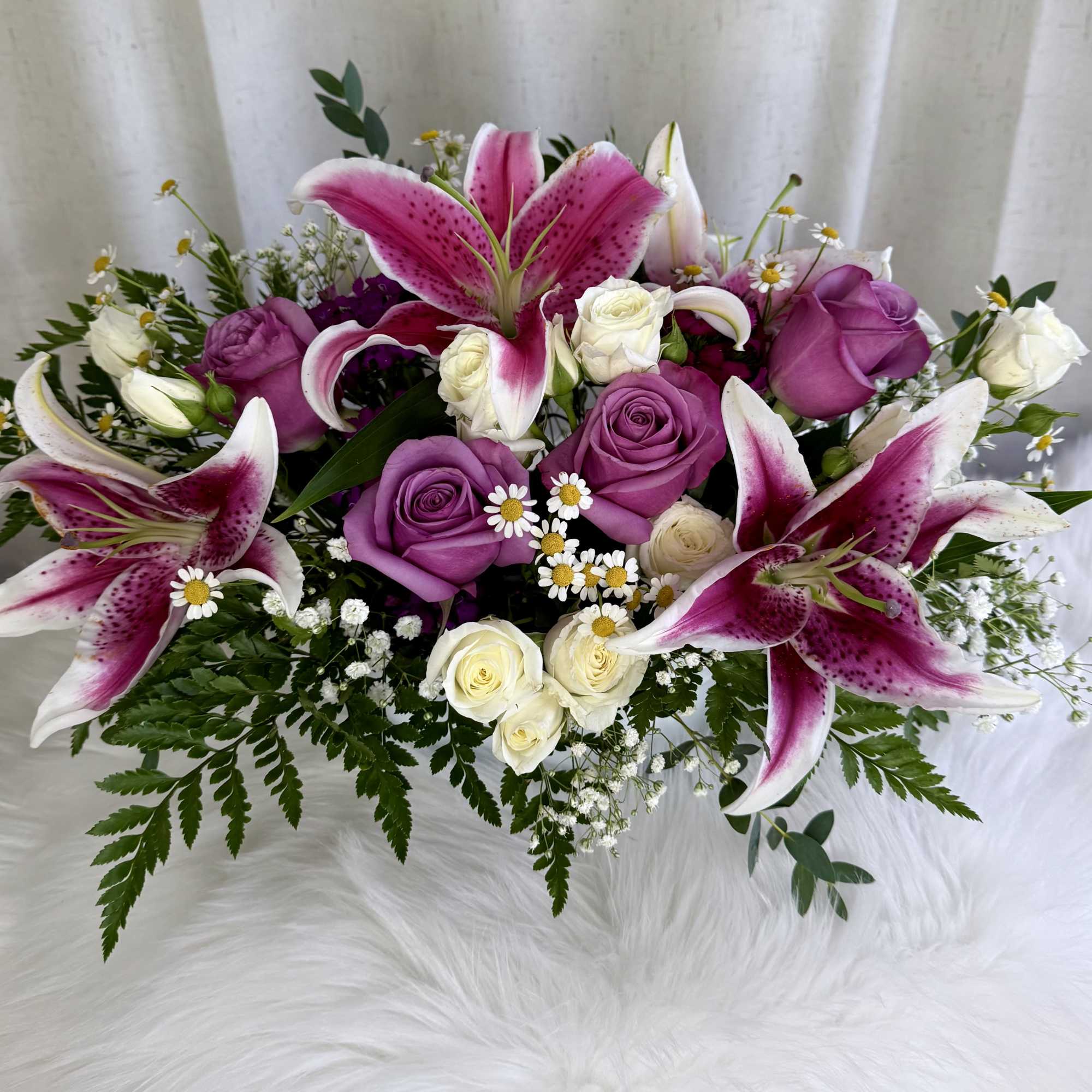 Pink lilies and purple roses arranged with small white flowers.