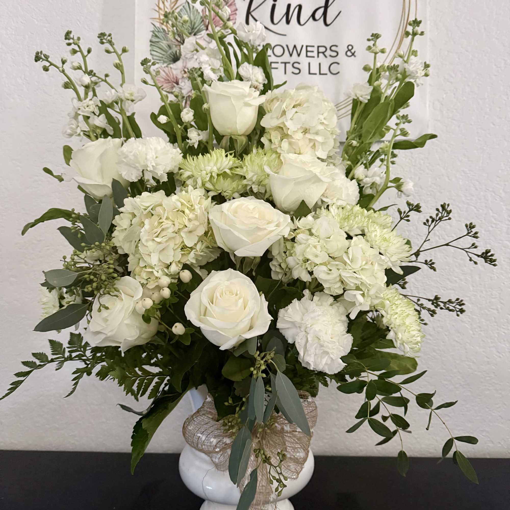 White roses and hydrangeas arranged in a white vase with greenery