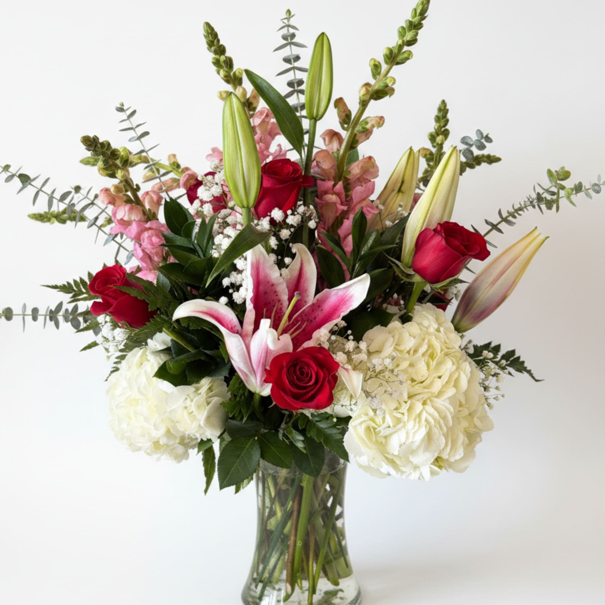 Bouquet of red roses, pink lilies, and white hydrangeas in a glass vase