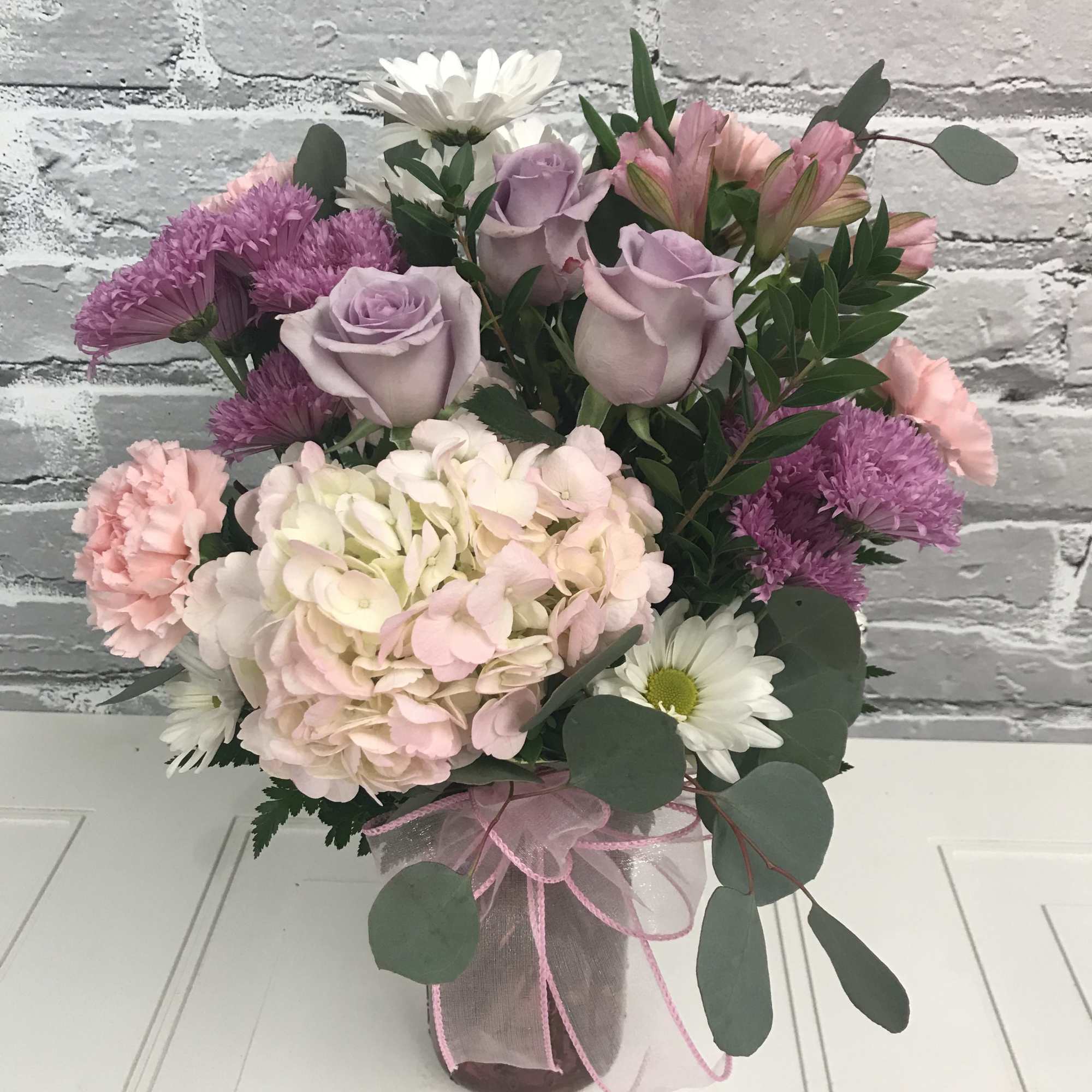 Pink and lavender bouquet in a glass vase with white daisies
