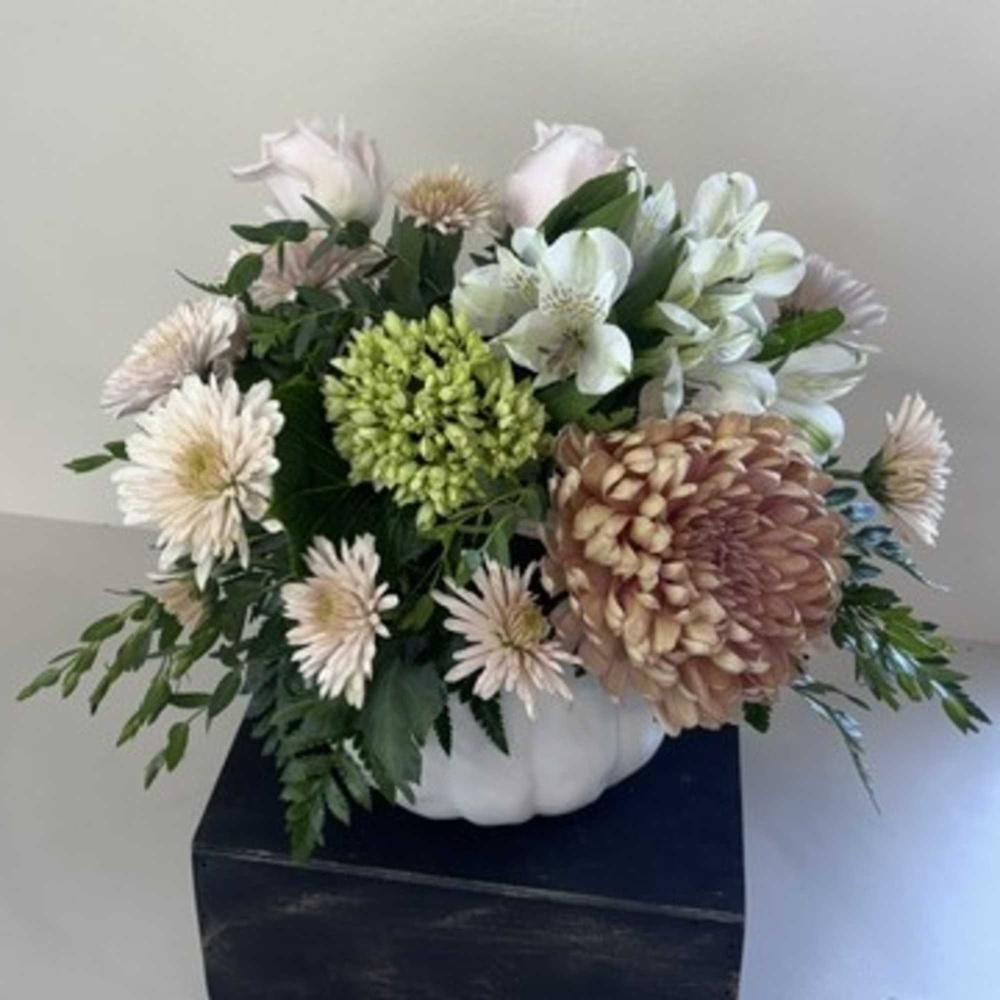 Floral arrangement in a white pumpkin-shaped container with pale blooms