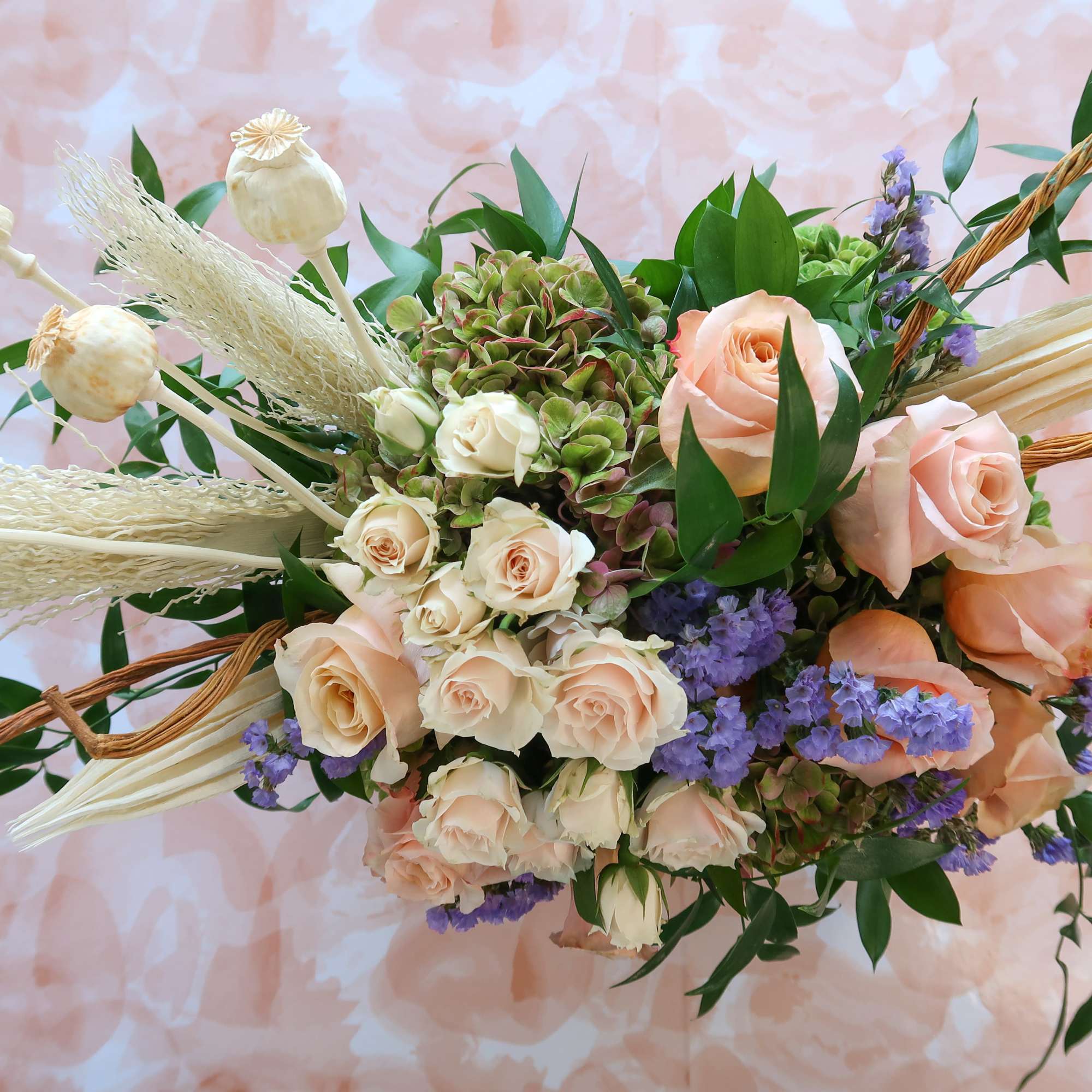 Asymmetrical bouquet of peach roses, spray roses, hydrangea and purple filler flowers with dried pods and grasses