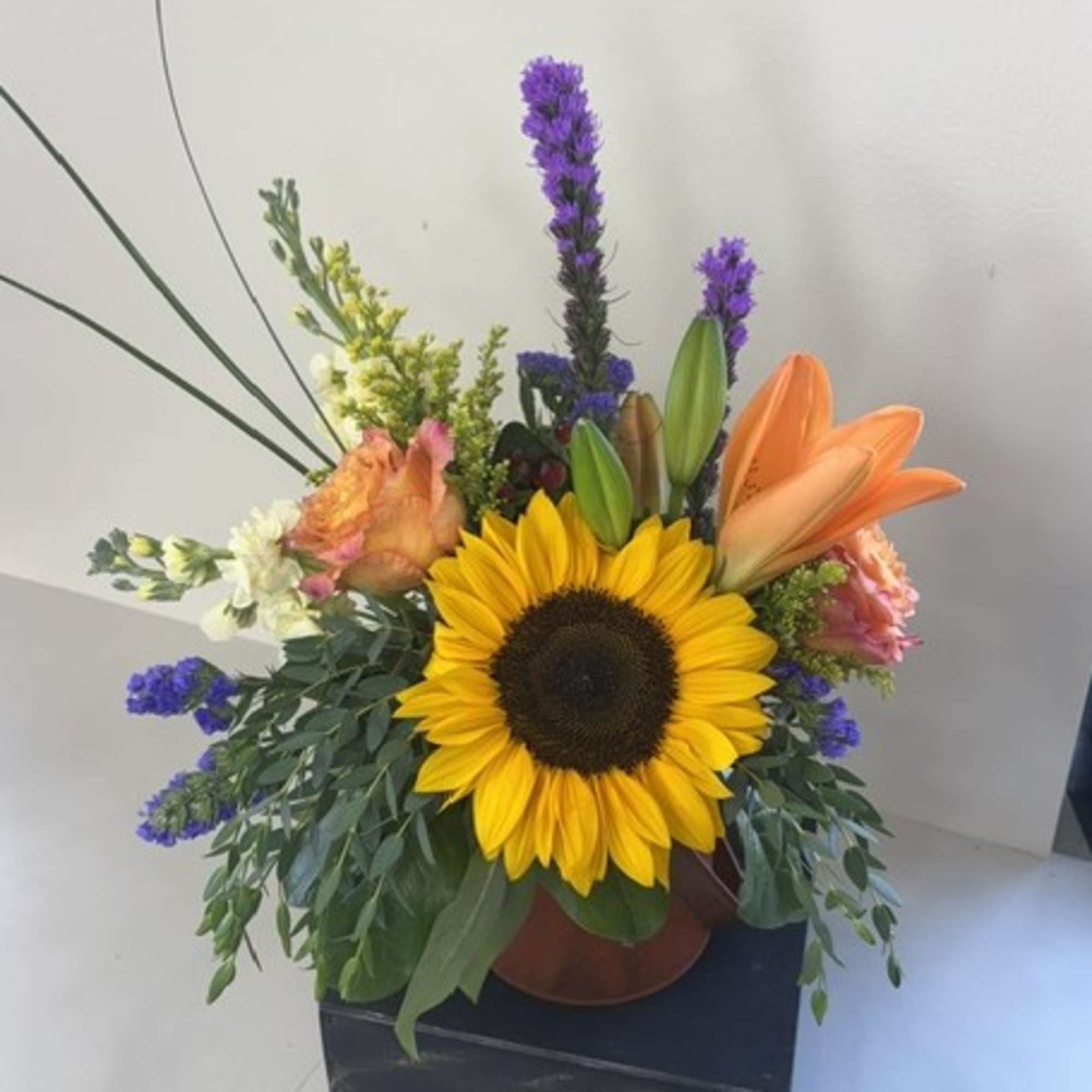 Sunflower arrangement with orange lilies and purple accents in a vase