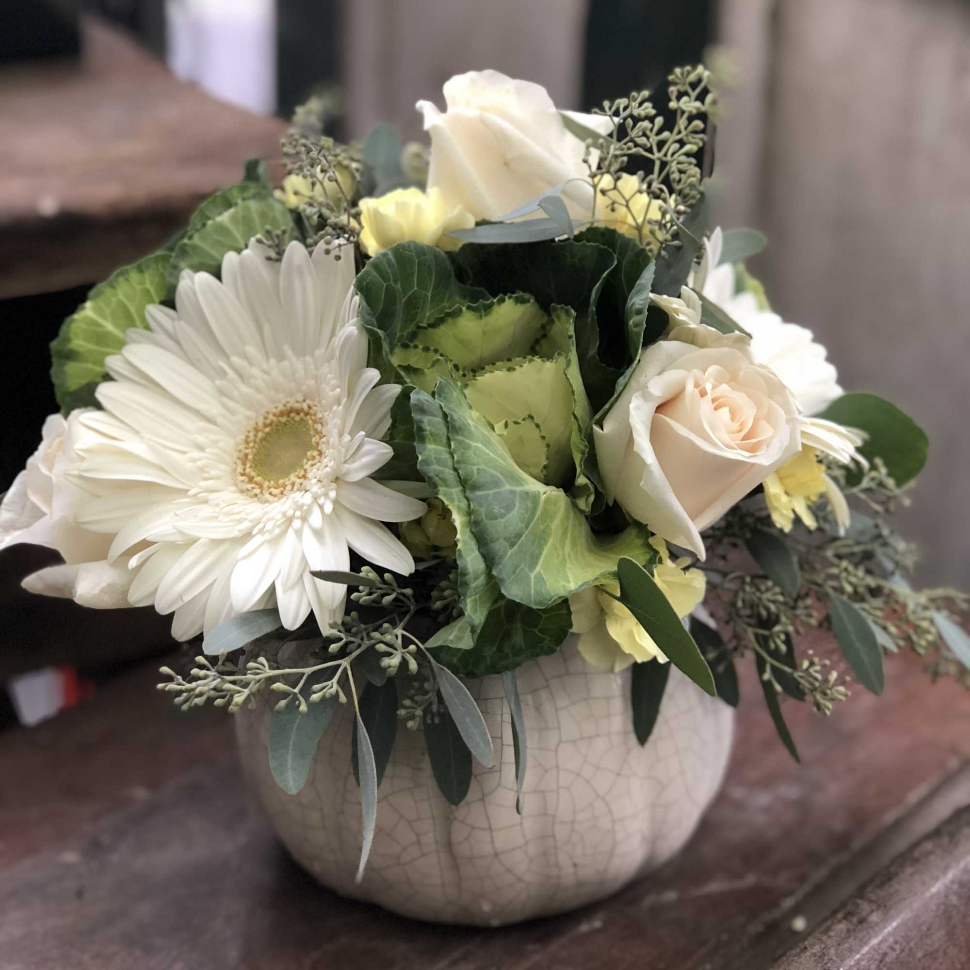 White gerbera daisies and pale roses arranged in a round vase