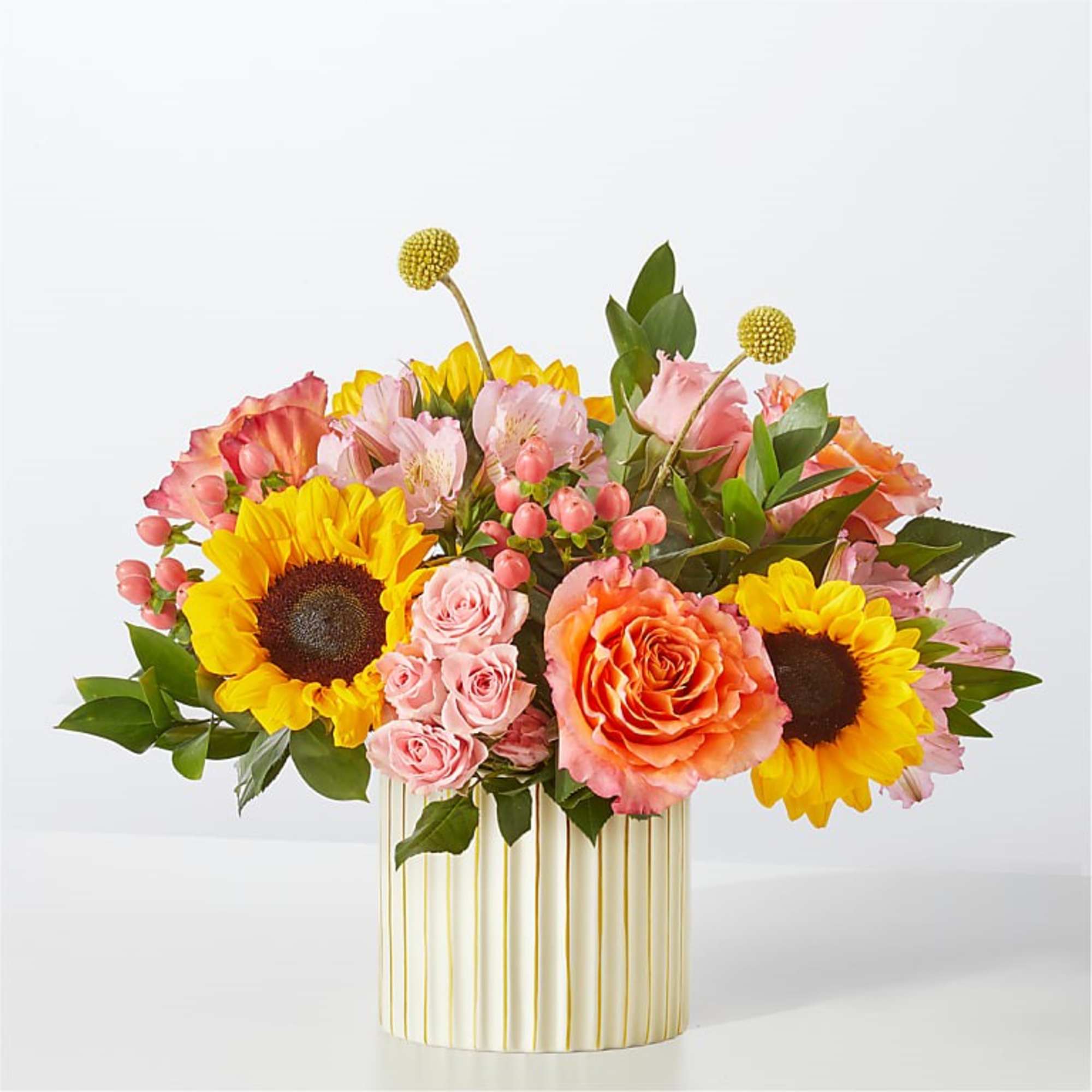 Mixed bouquet of sunflowers, roses, and pink blooms in a striped vase