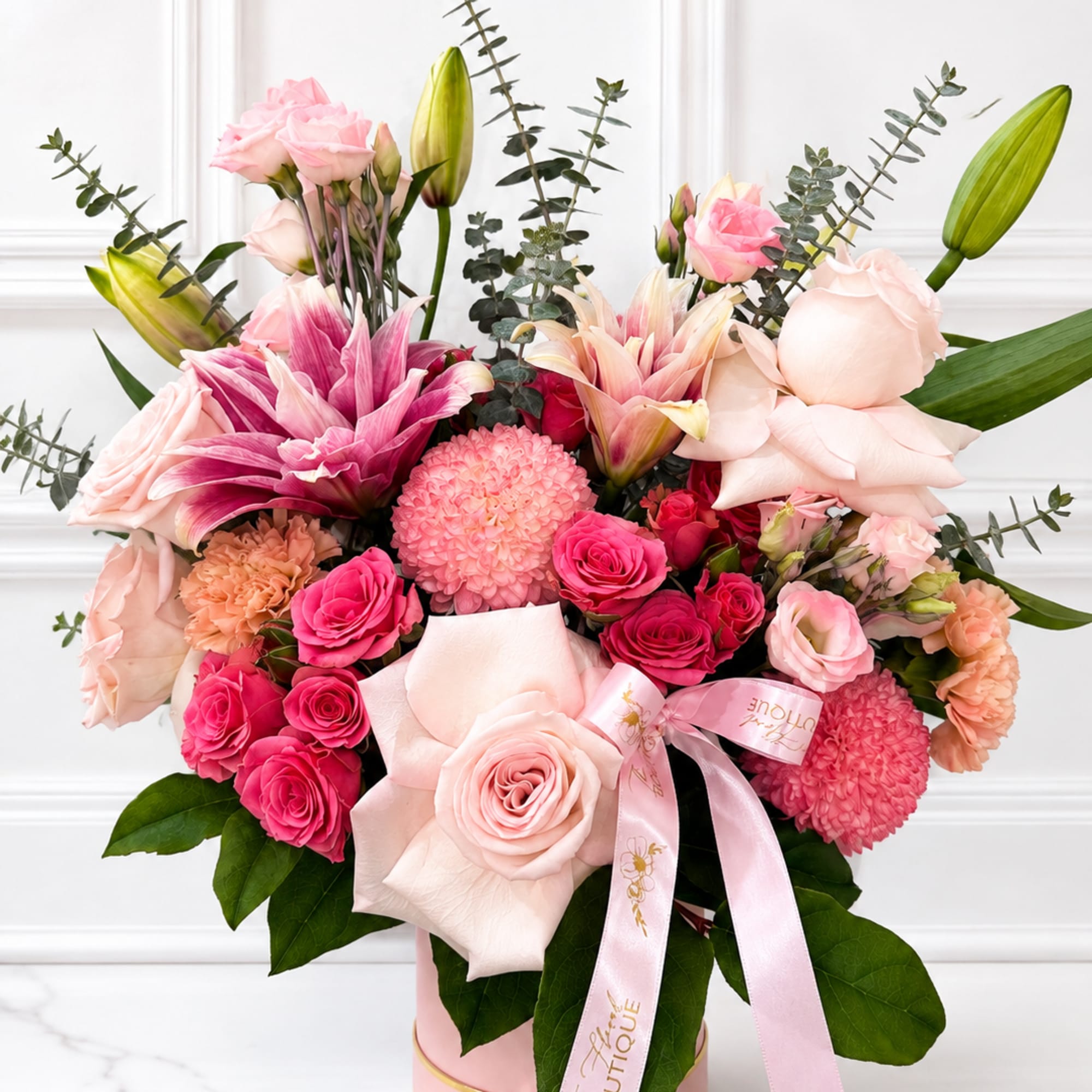 Pink and peach bouquet with roses, lilies, and a ribbon in a round box