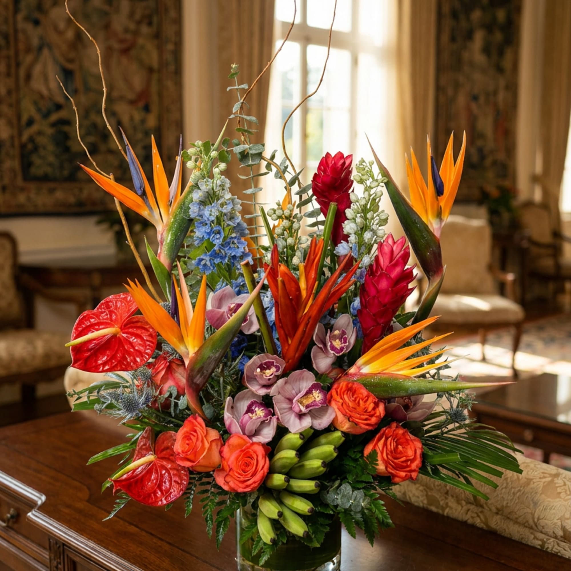 Tropical bouquet with orange bird-of-paradise, red anthuriums, and orchids in a glass vase.