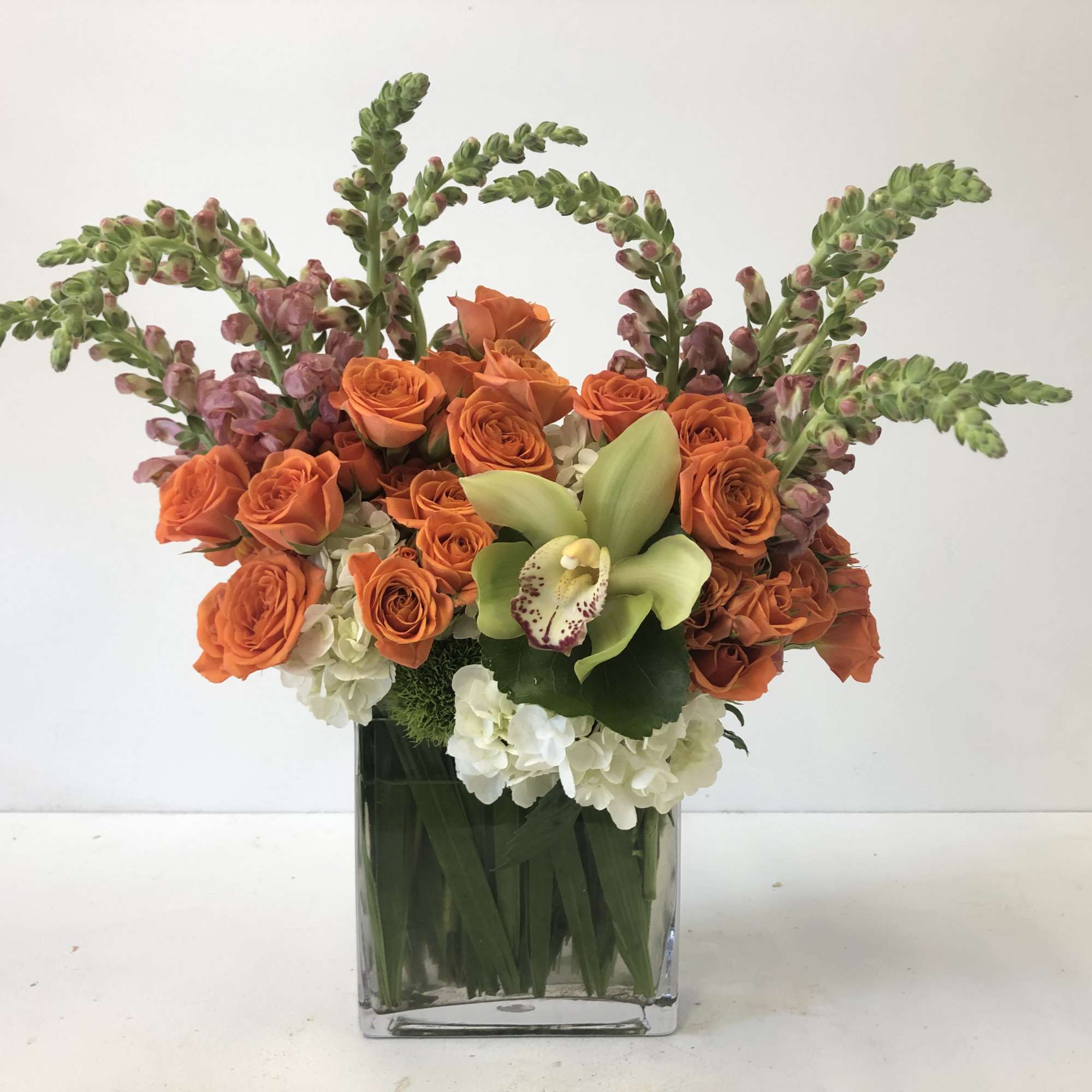 Orange roses and white blooms in a square glass vase