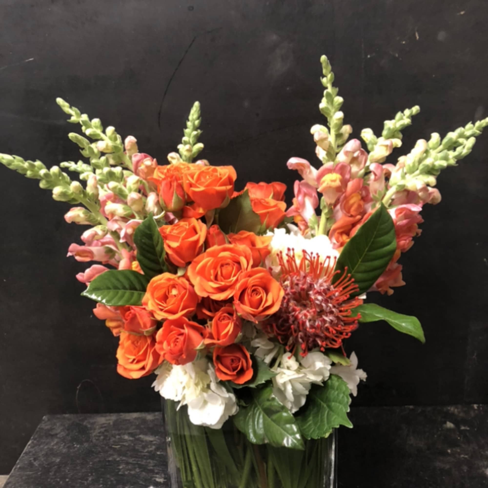 Orange roses and pink snapdragons in a square glass vase
