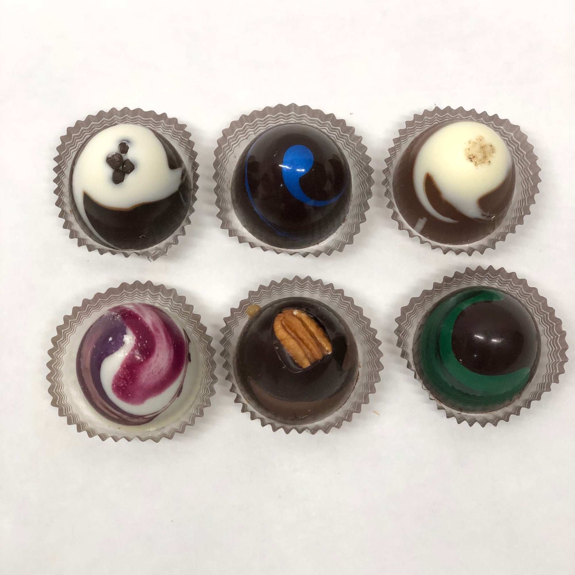 Set of six assorted round chocolates in individual cups on a white background