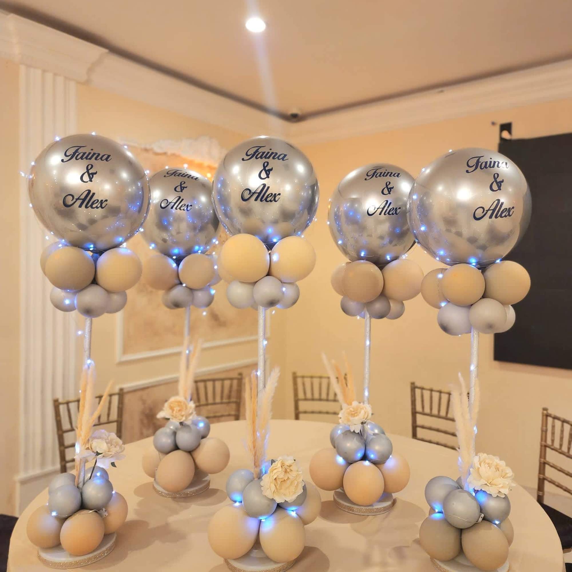 Silver balloons on stands with small cream floral accents on a table