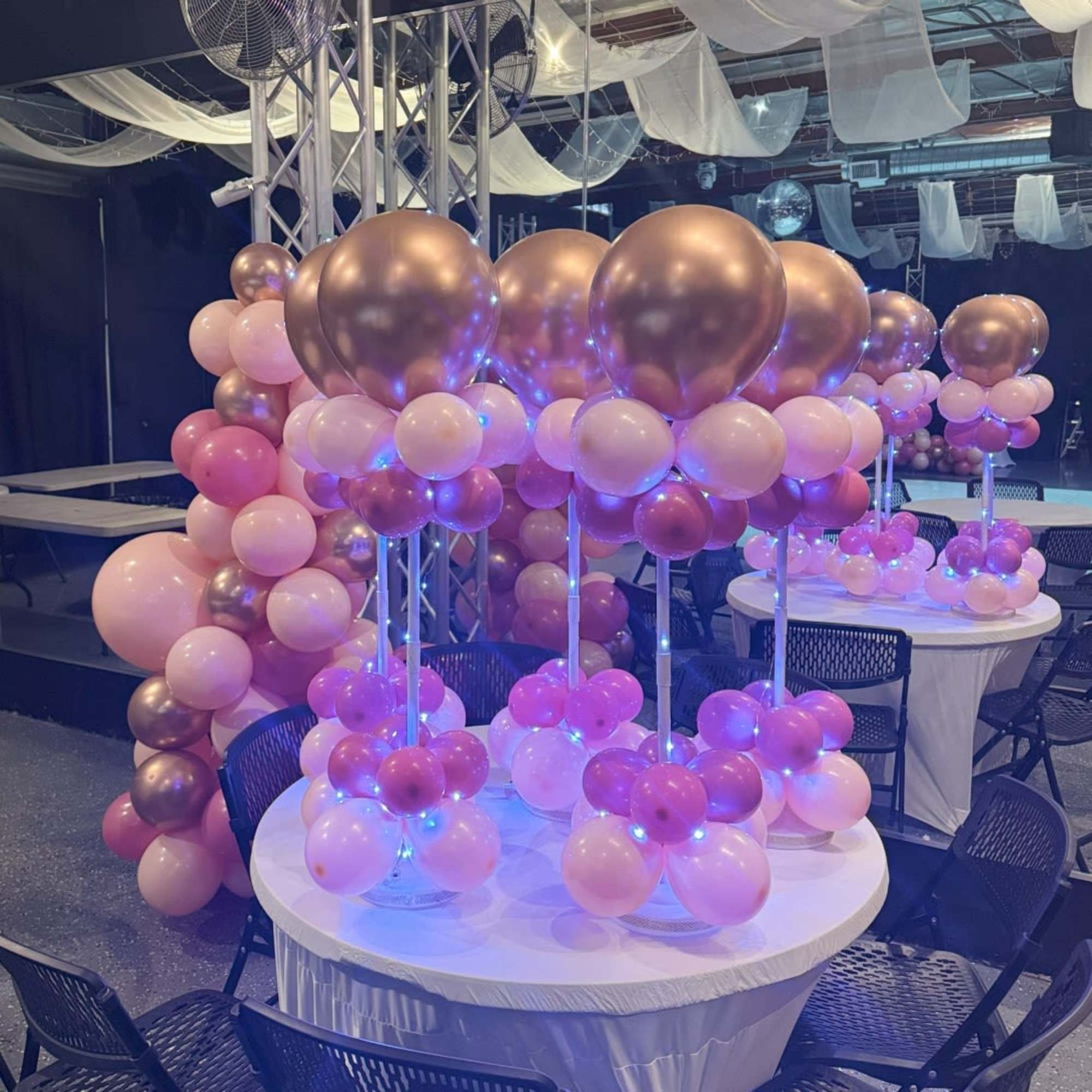 Pink and metallic balloon centerpieces on round tables in an event space