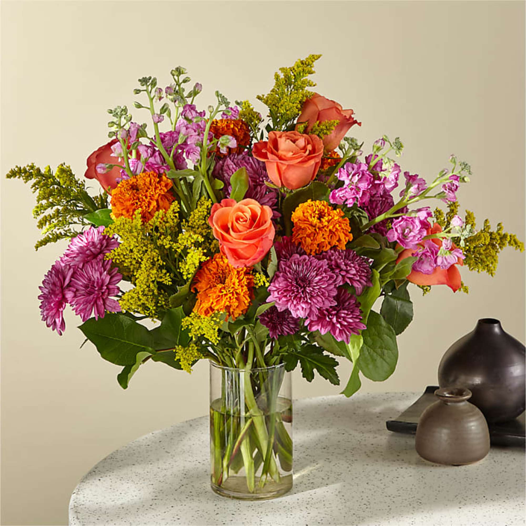 Mixed bouquet of orange roses, purple mums, and yellow filler in a clear glass vase