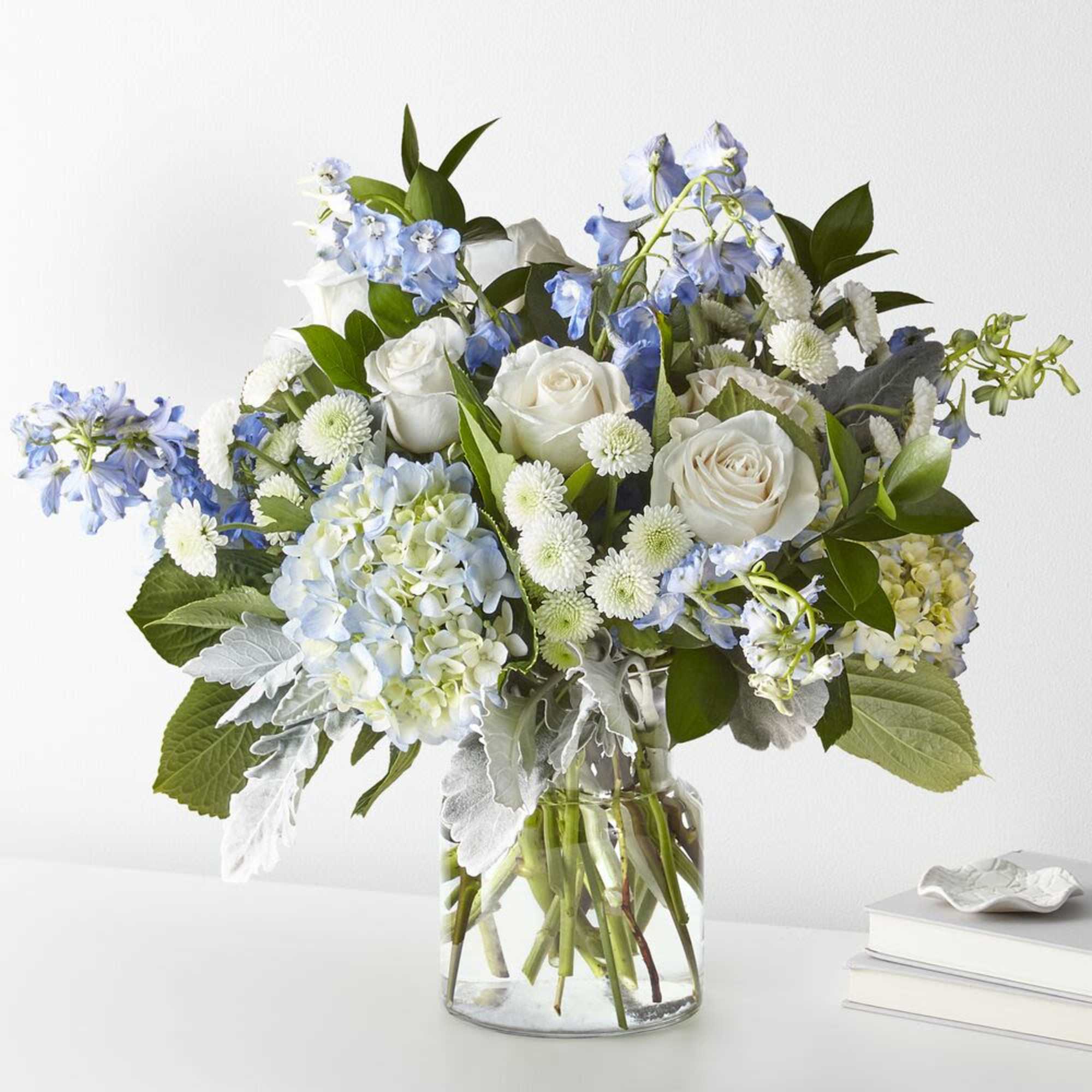 White roses and blue flowers arranged in a clear glass vase