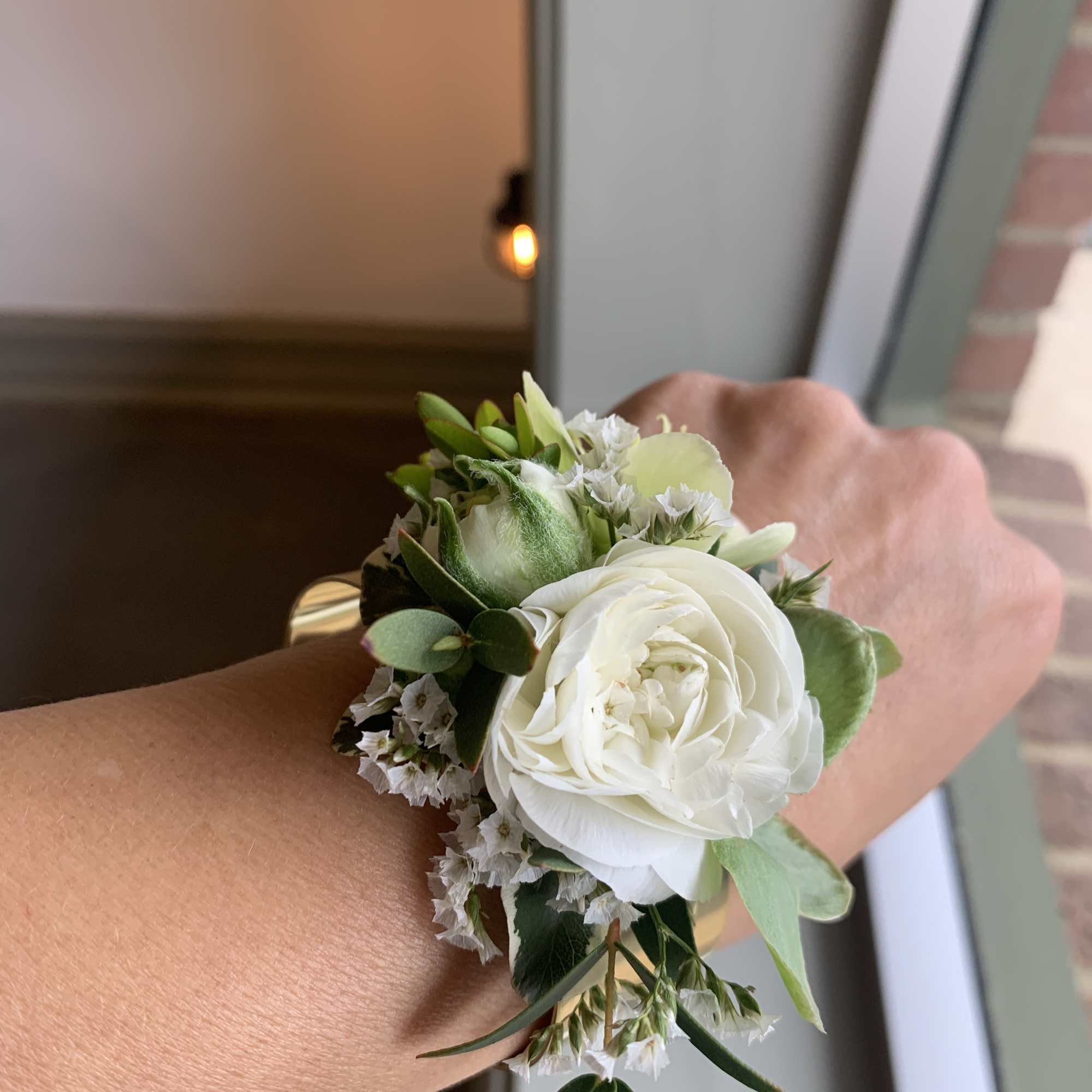 White floral wrist corsage with green accents on a wrist