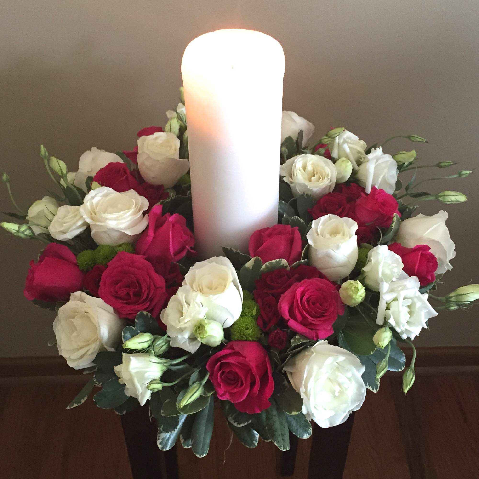 Red and white rose arrangement around a large white pillar candle