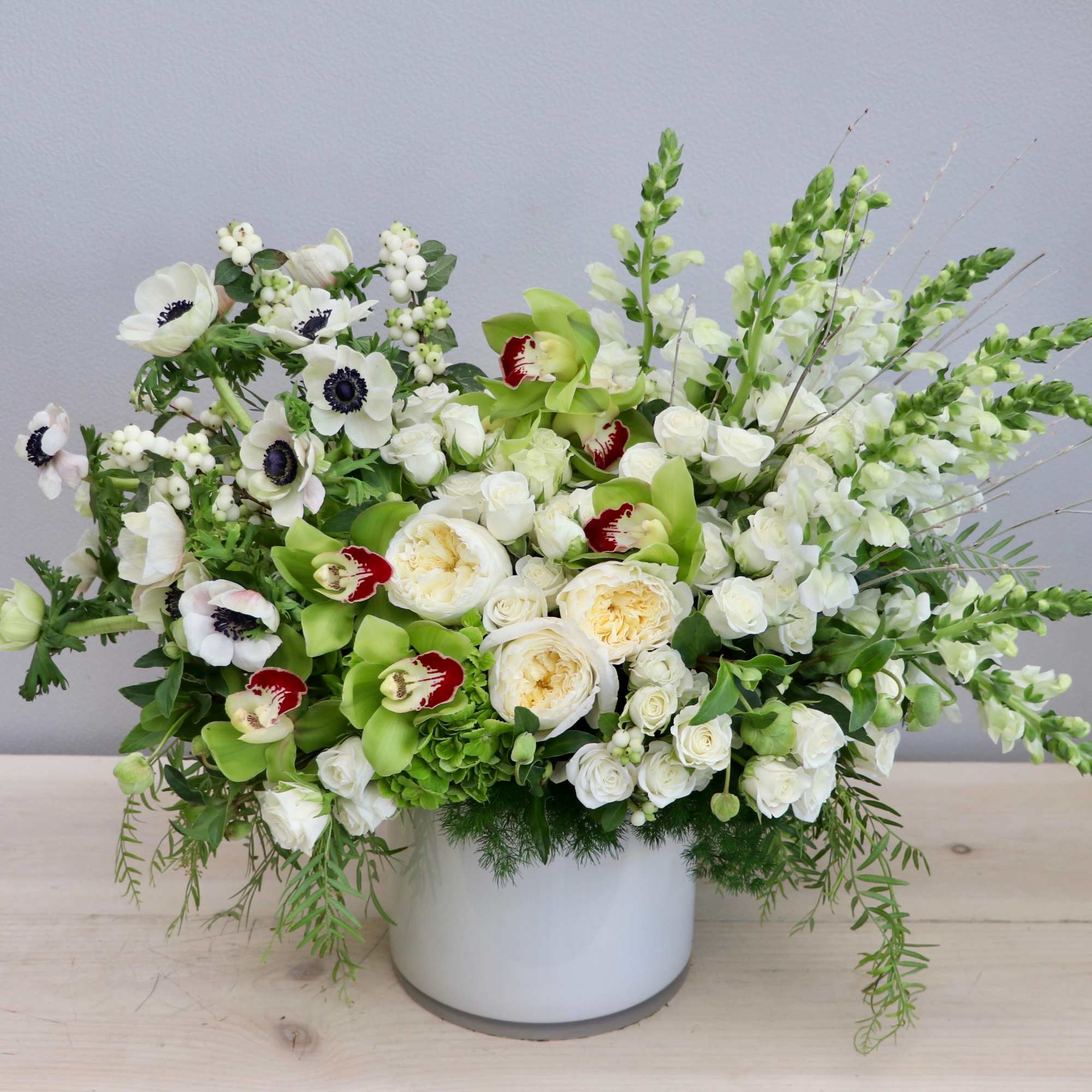 Low white vase with white blooms, green orchids, and cream roses in an airy arrangement