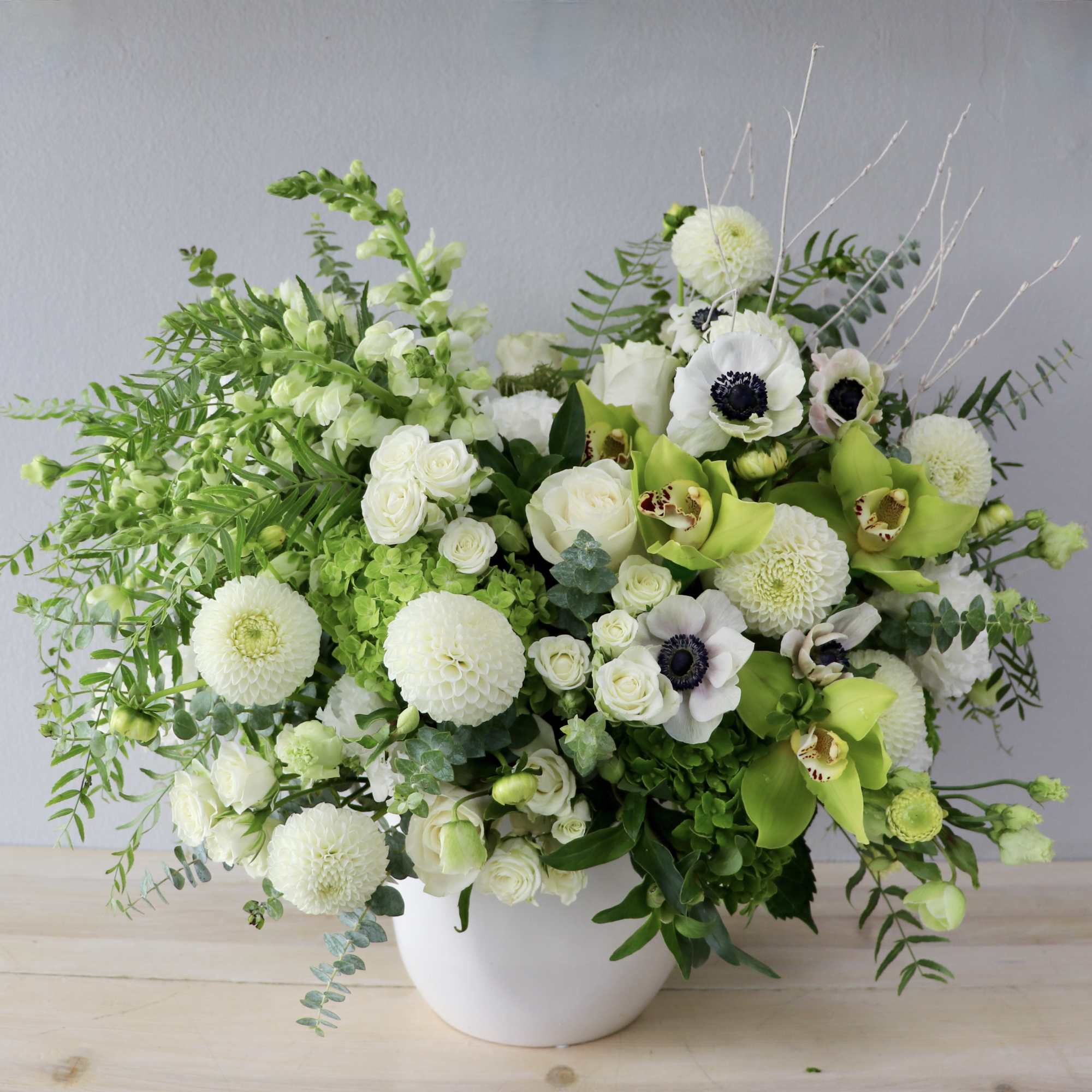 White and green floral arrangement in a white vase with round blooms and orchids