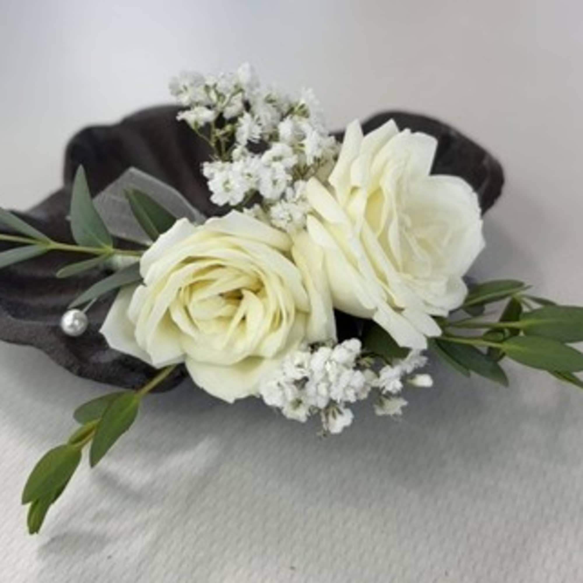 White rose boutonniere with small white filler flowers and dark green leaves