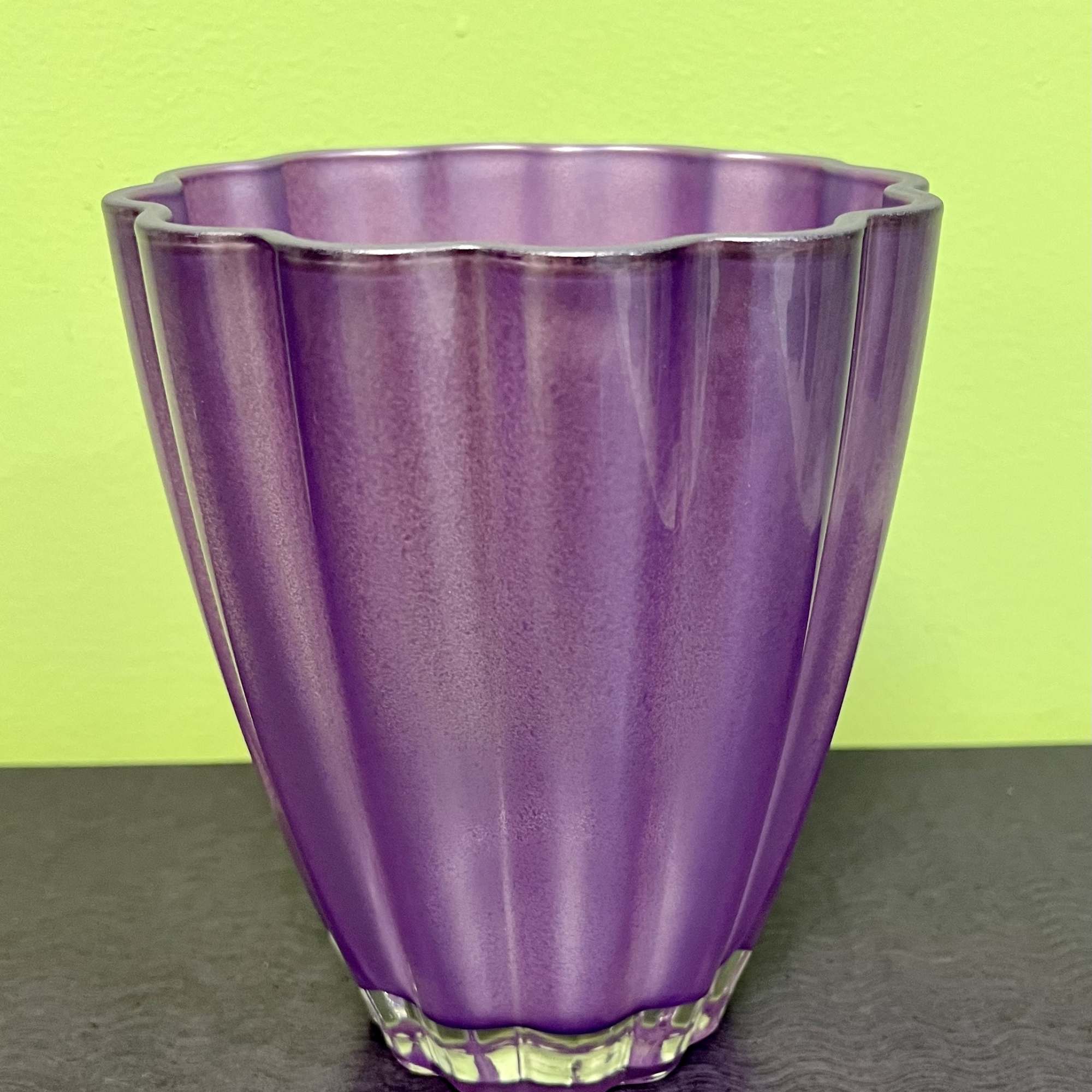 Purple glass vase with a scalloped rim on a dark surface