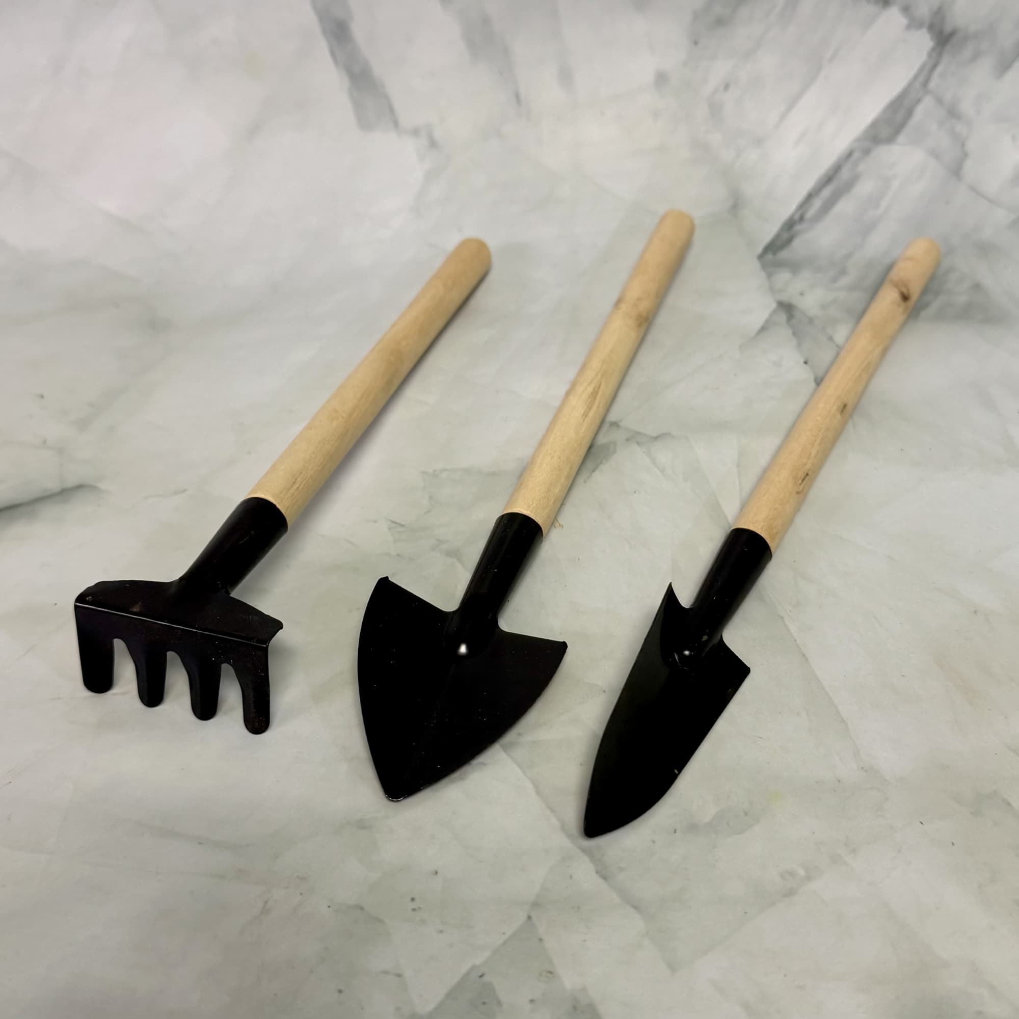 Three small gardening hand tools with wooden handles on a marble surface