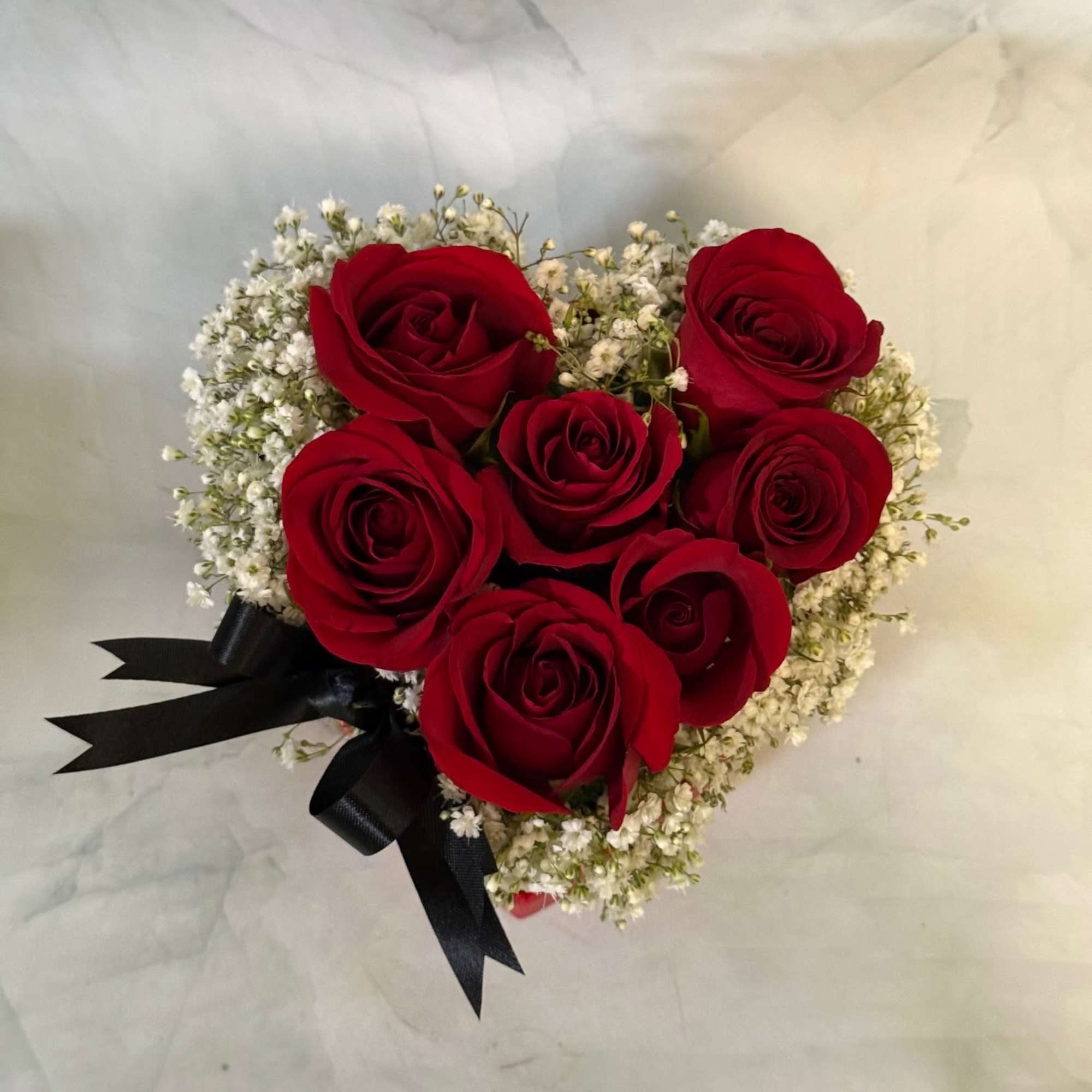Heart-shaped bouquet of red roses with white baby's breath and a black ribbon