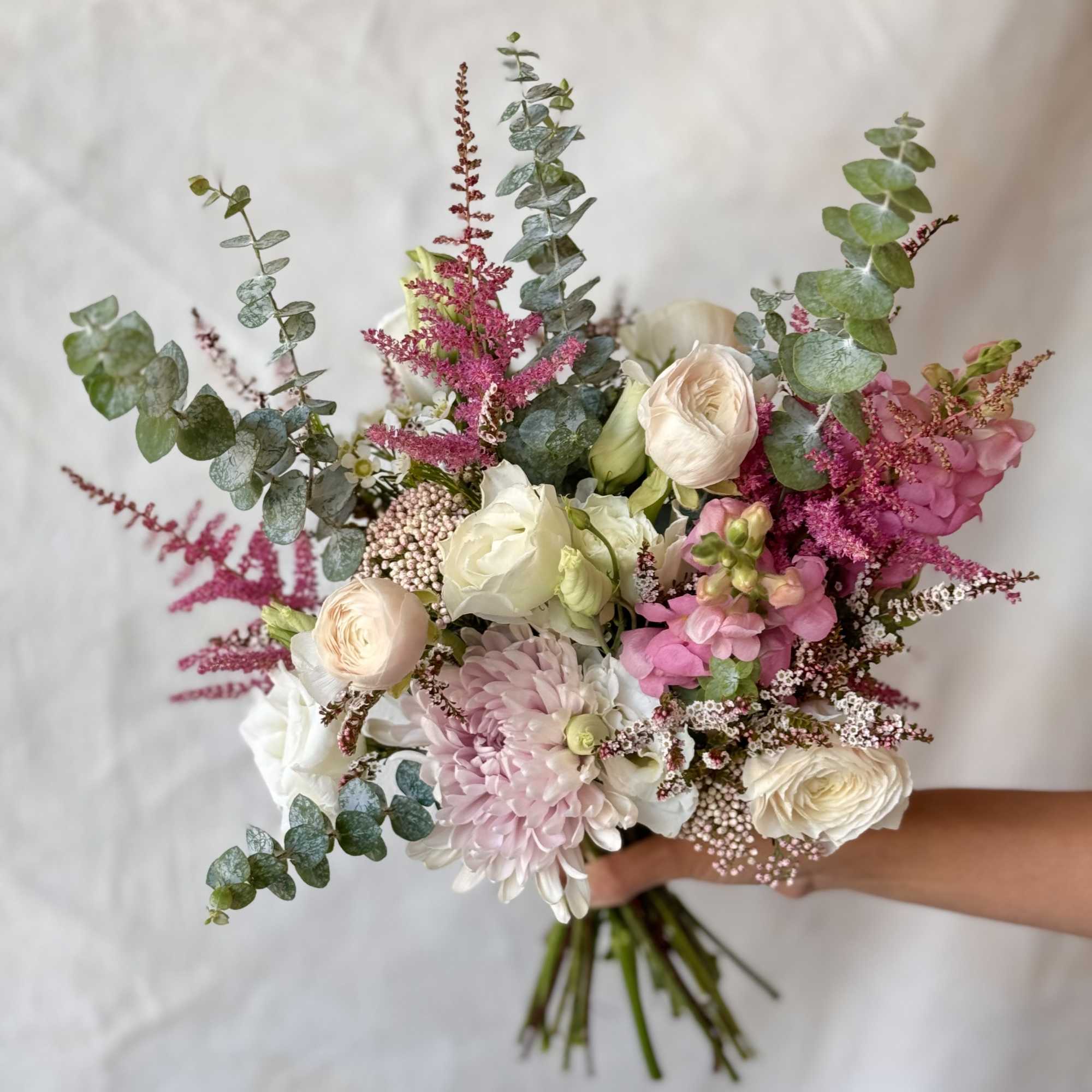 Handheld bouquet of blush, white, and pink flowers with eucalyptus