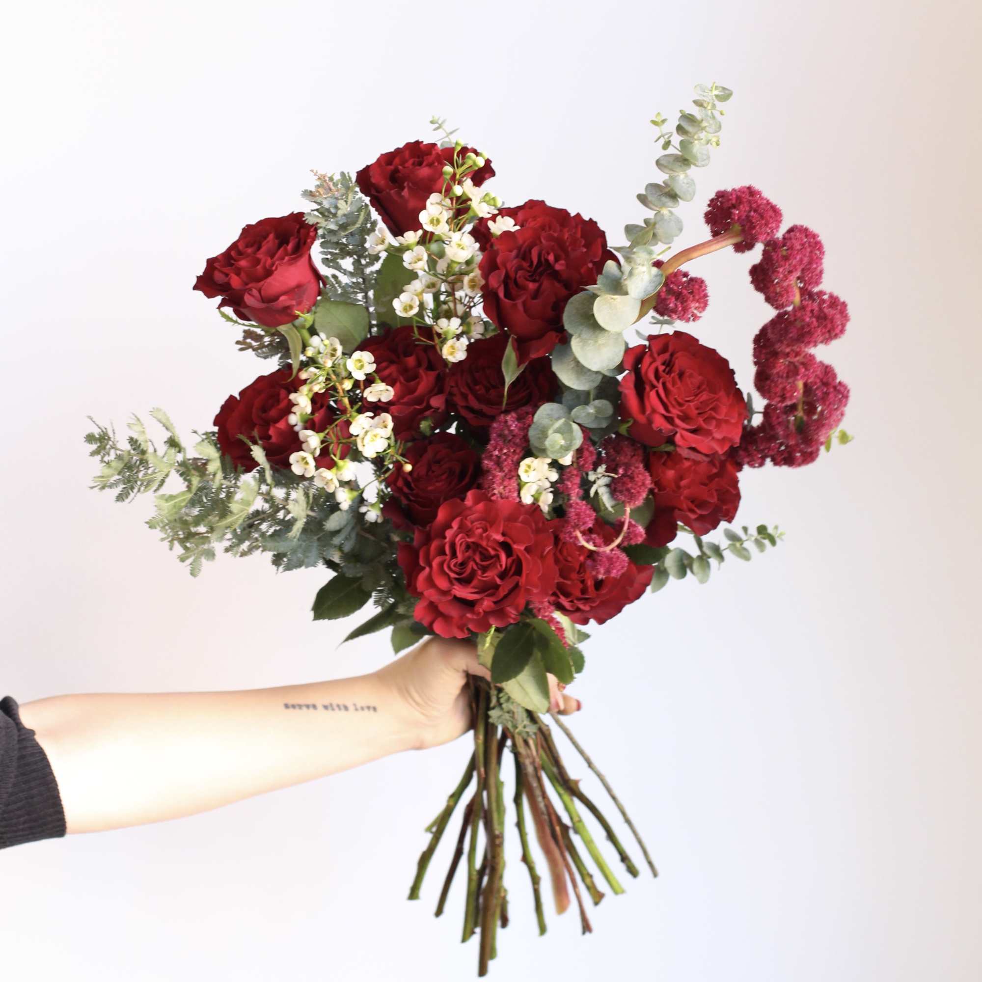 Handheld bouquet of red roses with white filler flowers and eucalyptus