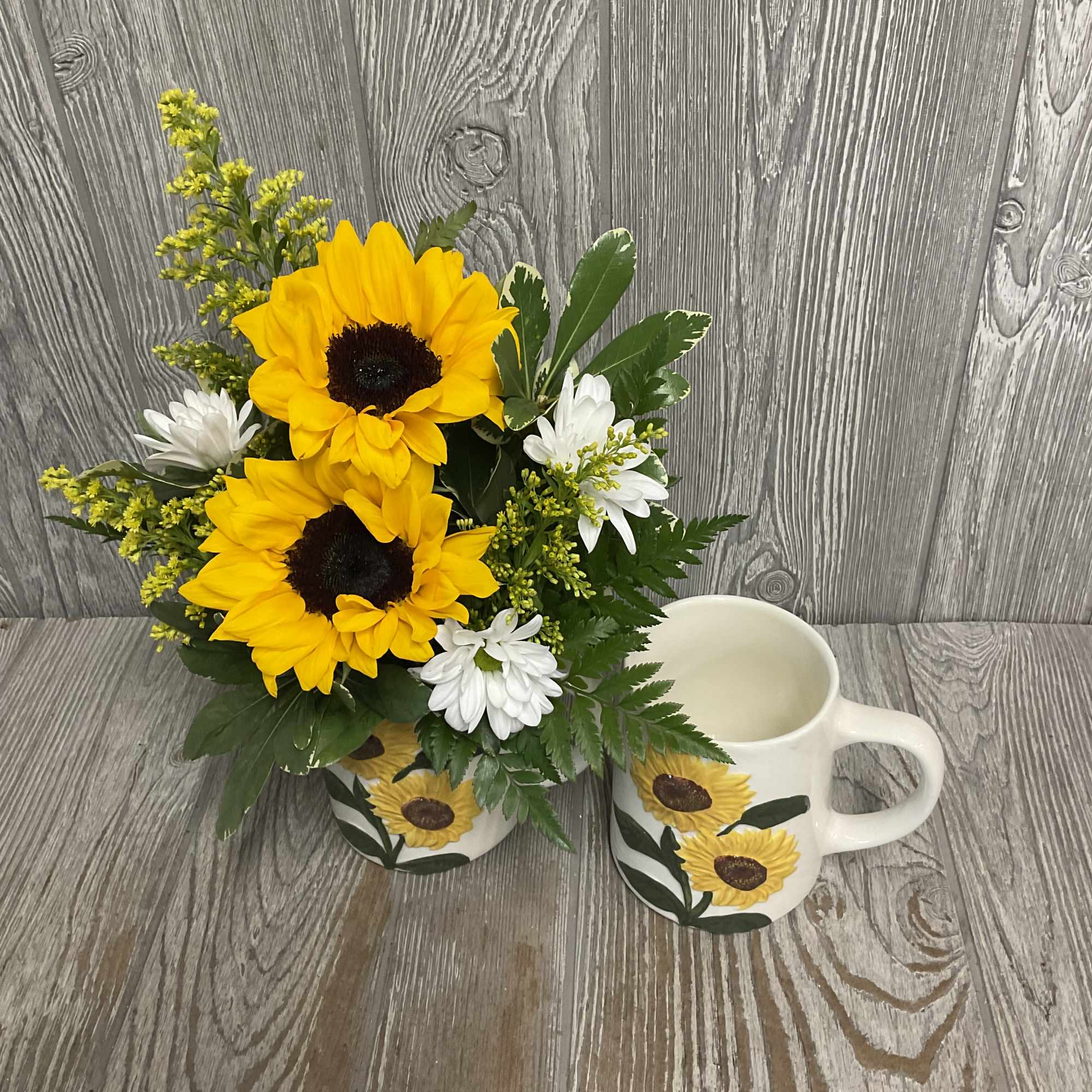 Sunflower bouquet in a painted mug beside a matching sunflower mug