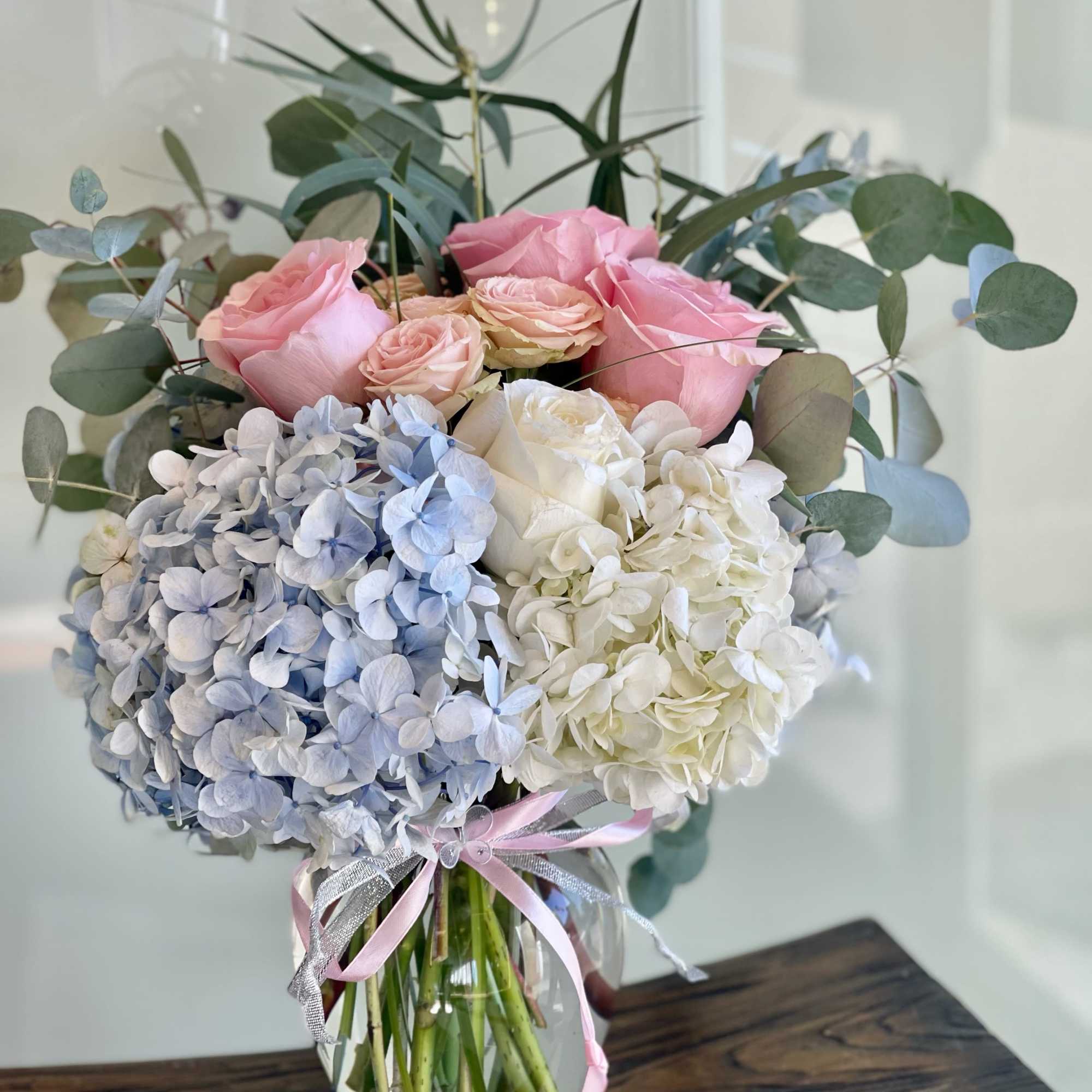 Pink roses and blue-white hydrangeas in a glass vase with ribbon