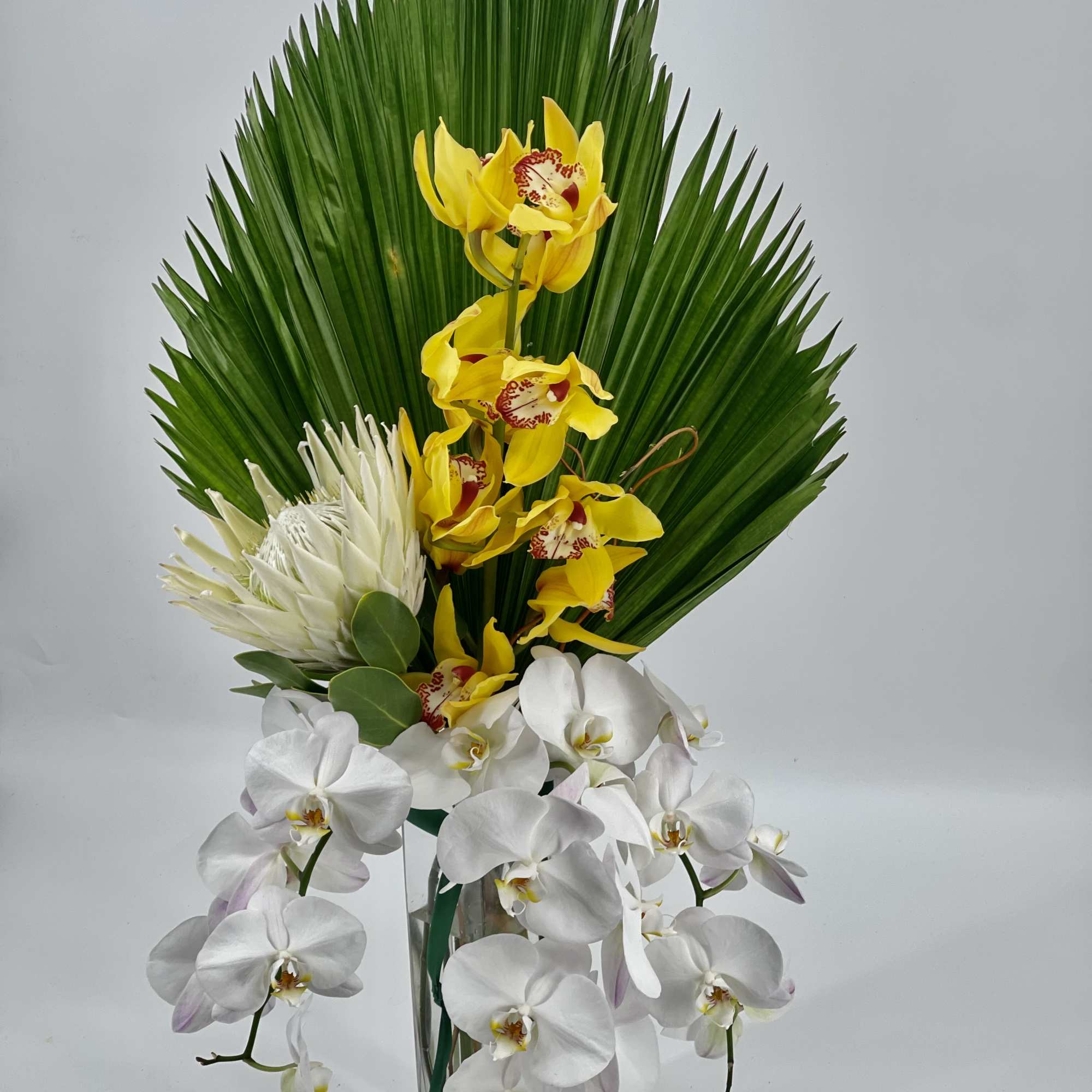 Yellow orchids and white orchids in a clear glass vase with large green palm leaves