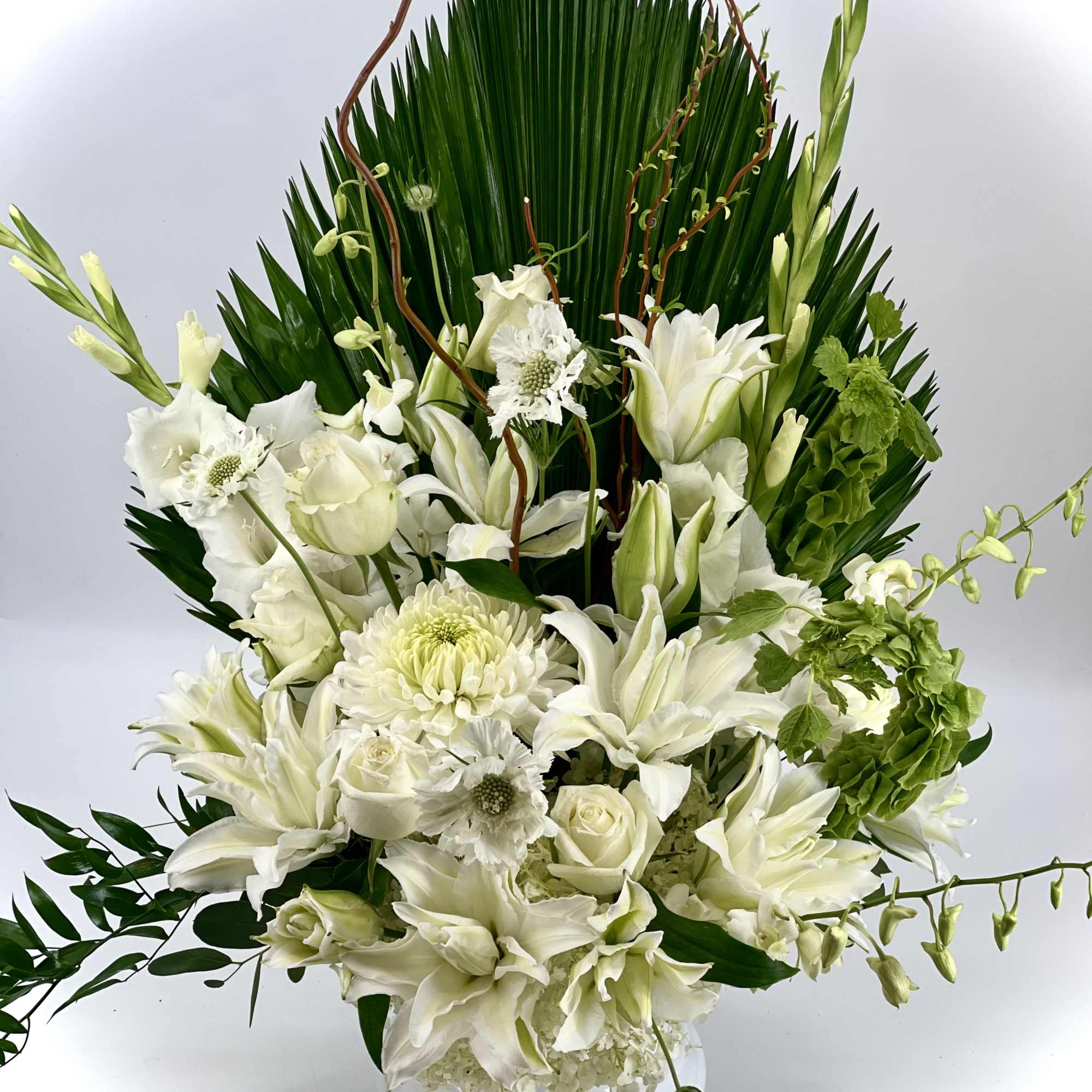 White floral arrangement in a clear glass vase with tall green foliage, photo 2 of 4