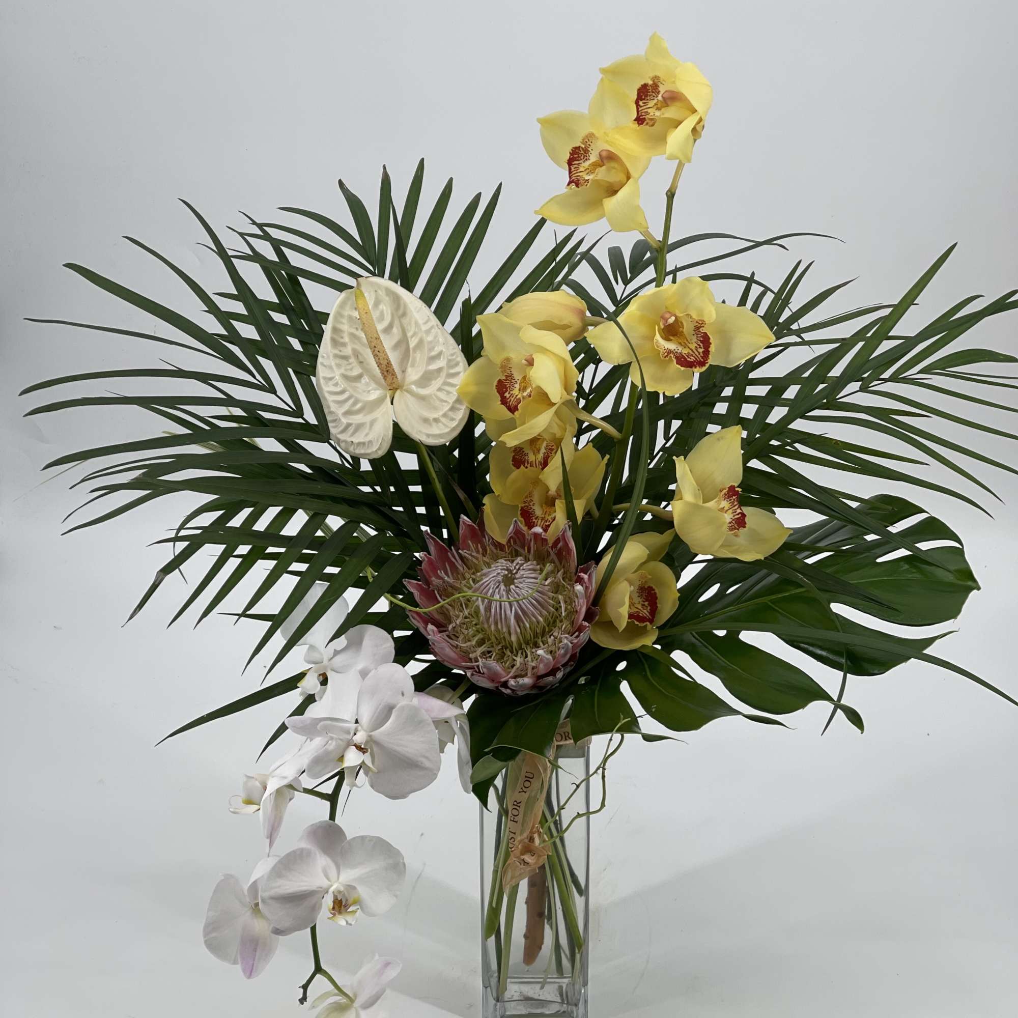Yellow and white orchids arranged in a tall glass vase with tropical foliage
