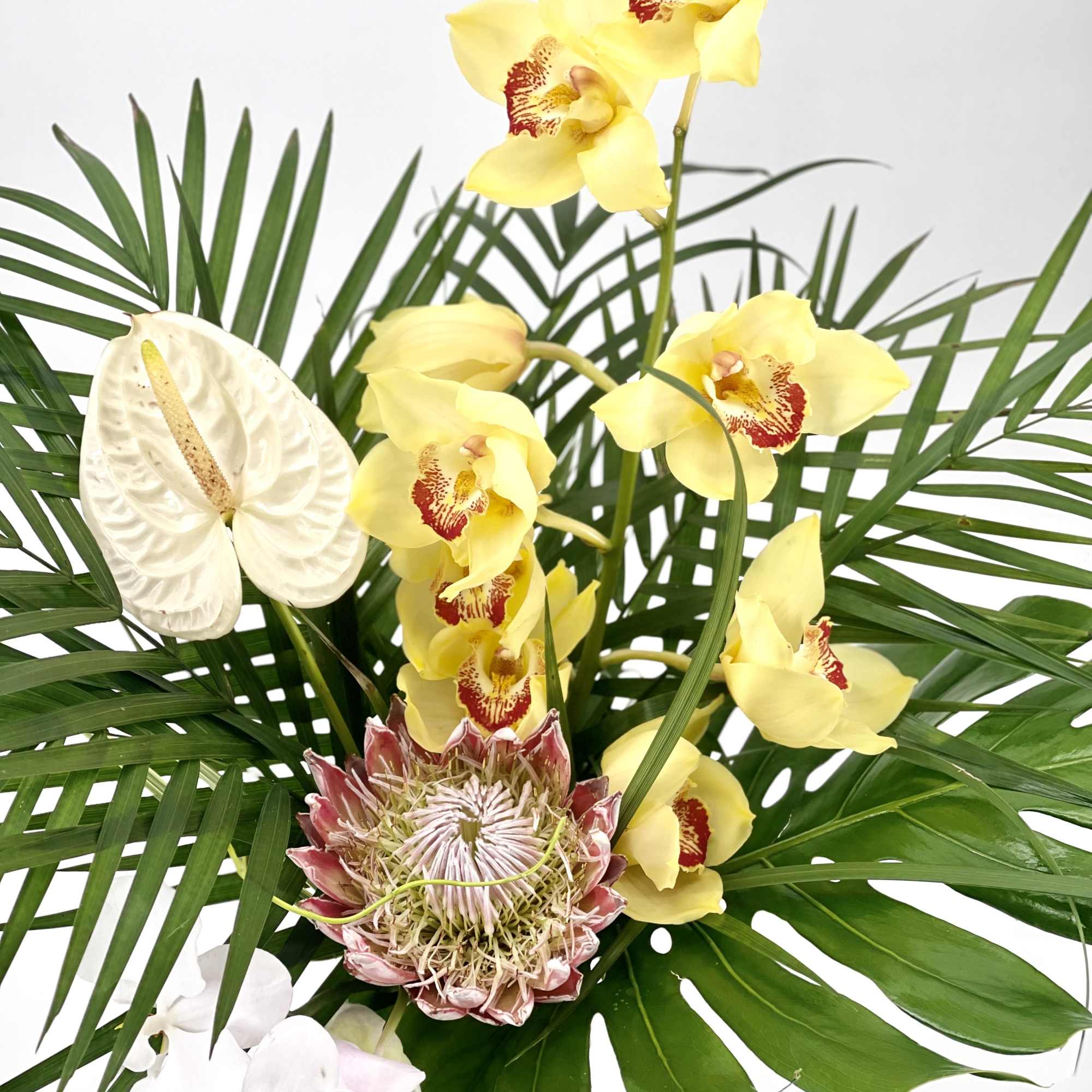 Tropical bouquet with yellow and white orchids and palm leaves