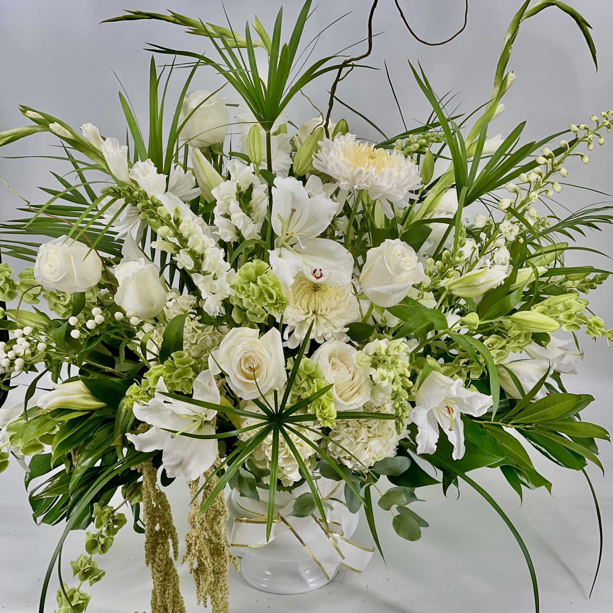White floral arrangement in a clear glass vase with long green foliage