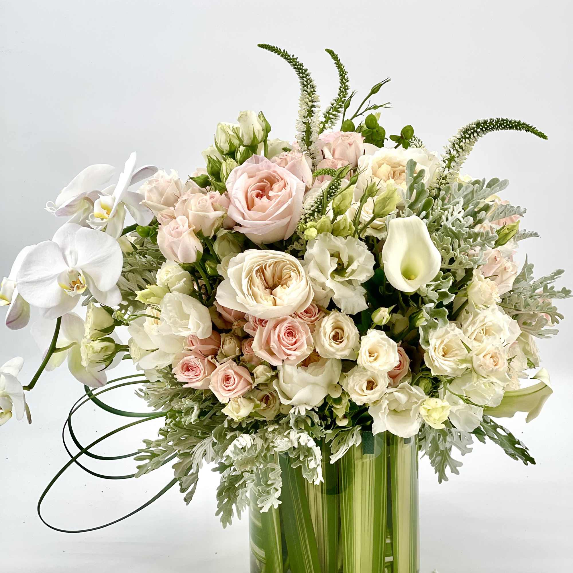 Pastel bouquet of roses, orchids, and calla lilies in a green glass vase