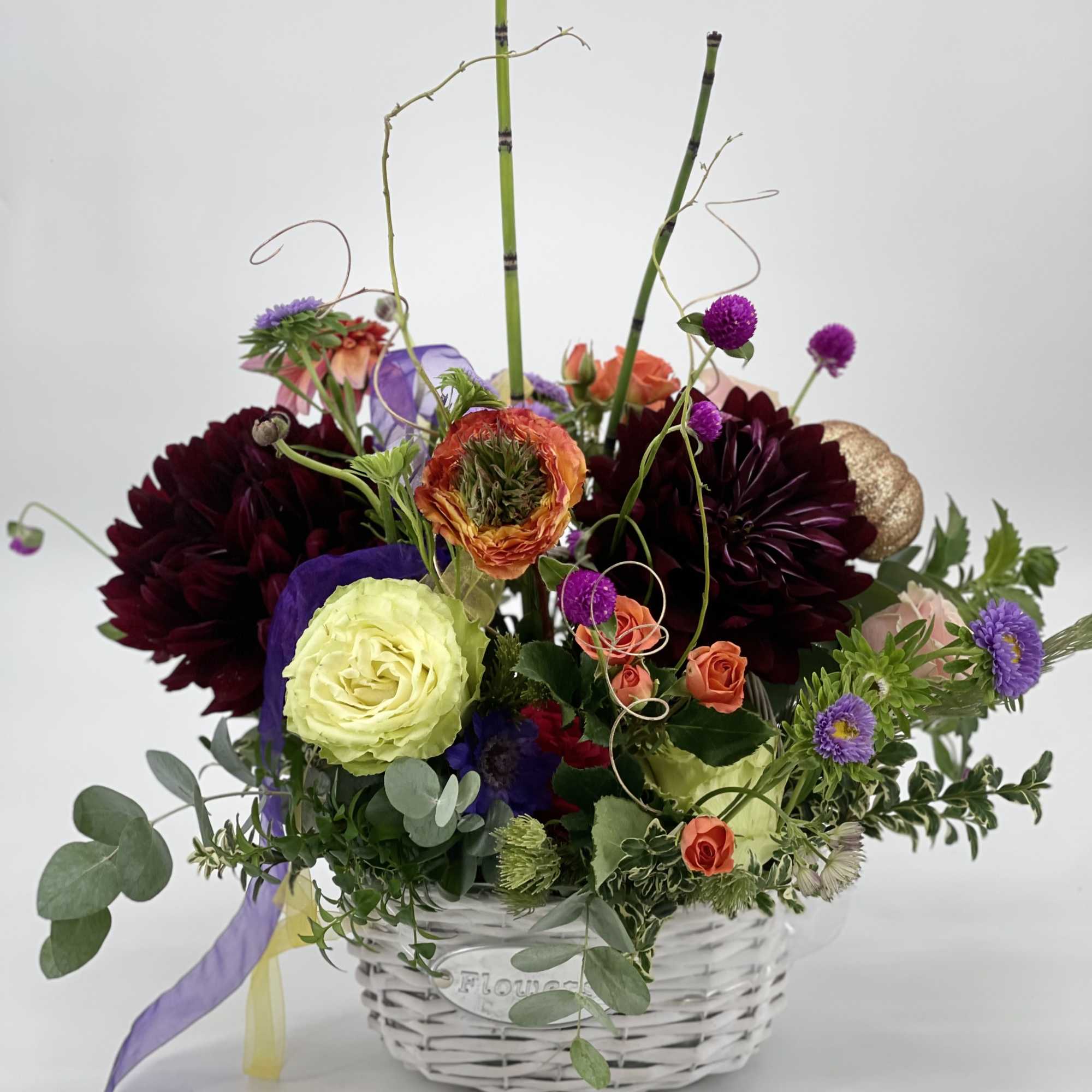 Mixed flower arrangement in a white wicker basket with tall bamboo stems