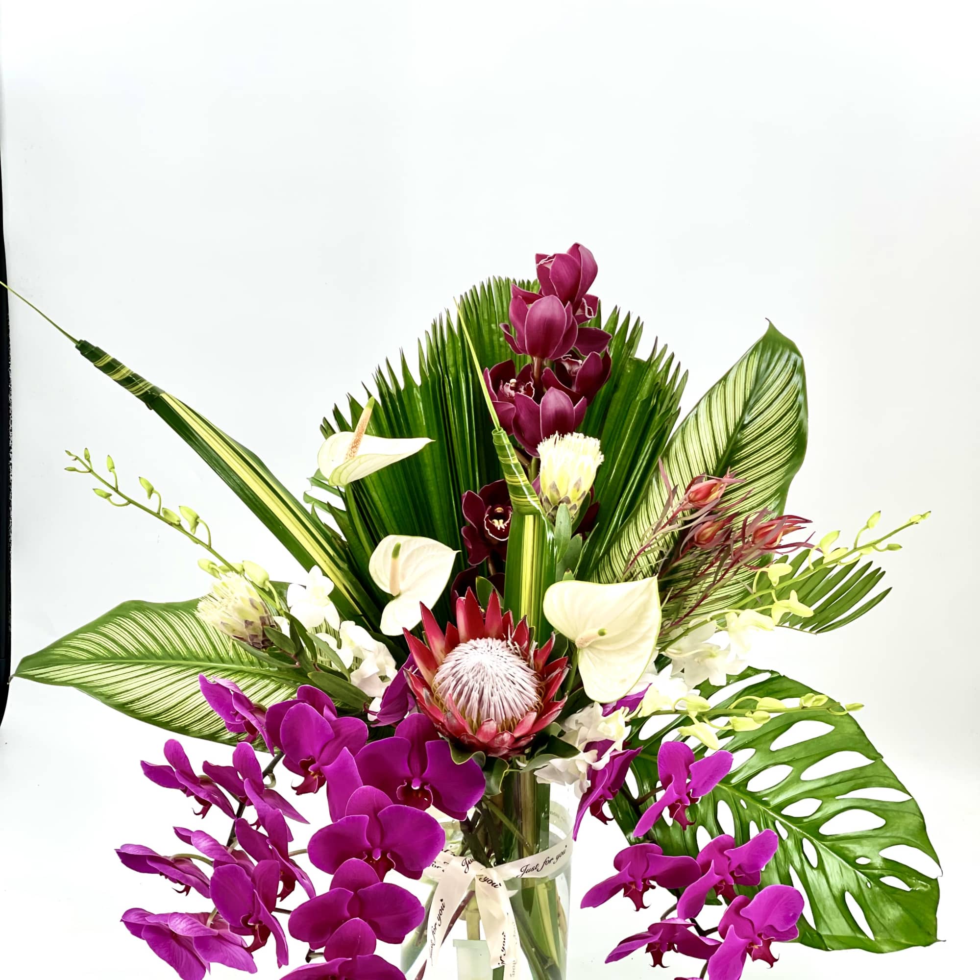 Tropical orchid arrangement in a glass vase with large green leaves