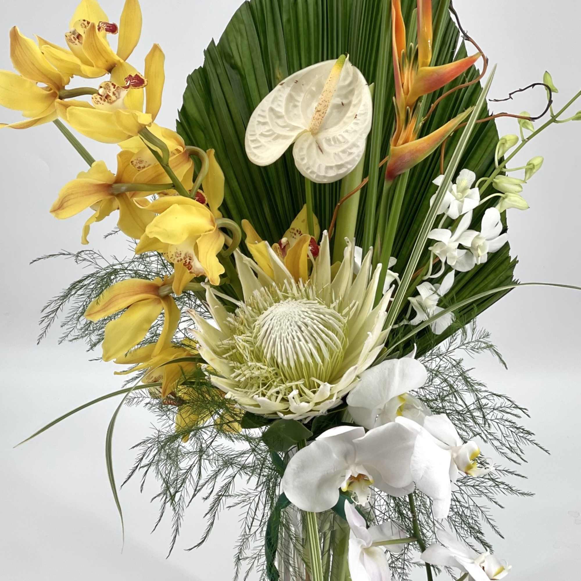 Tropical flower arrangement with yellow and white orchids in a clear vase